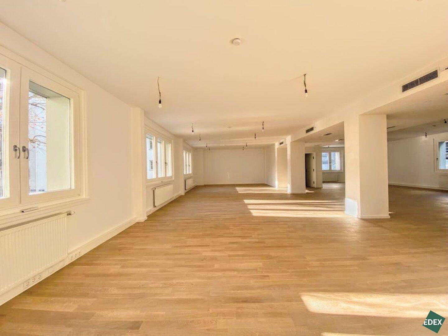 Weitläufiger, heller Raum mit vielen Fenstern und Holzparkett, bietet vielseitige Nutzungsmöglichkeiten.