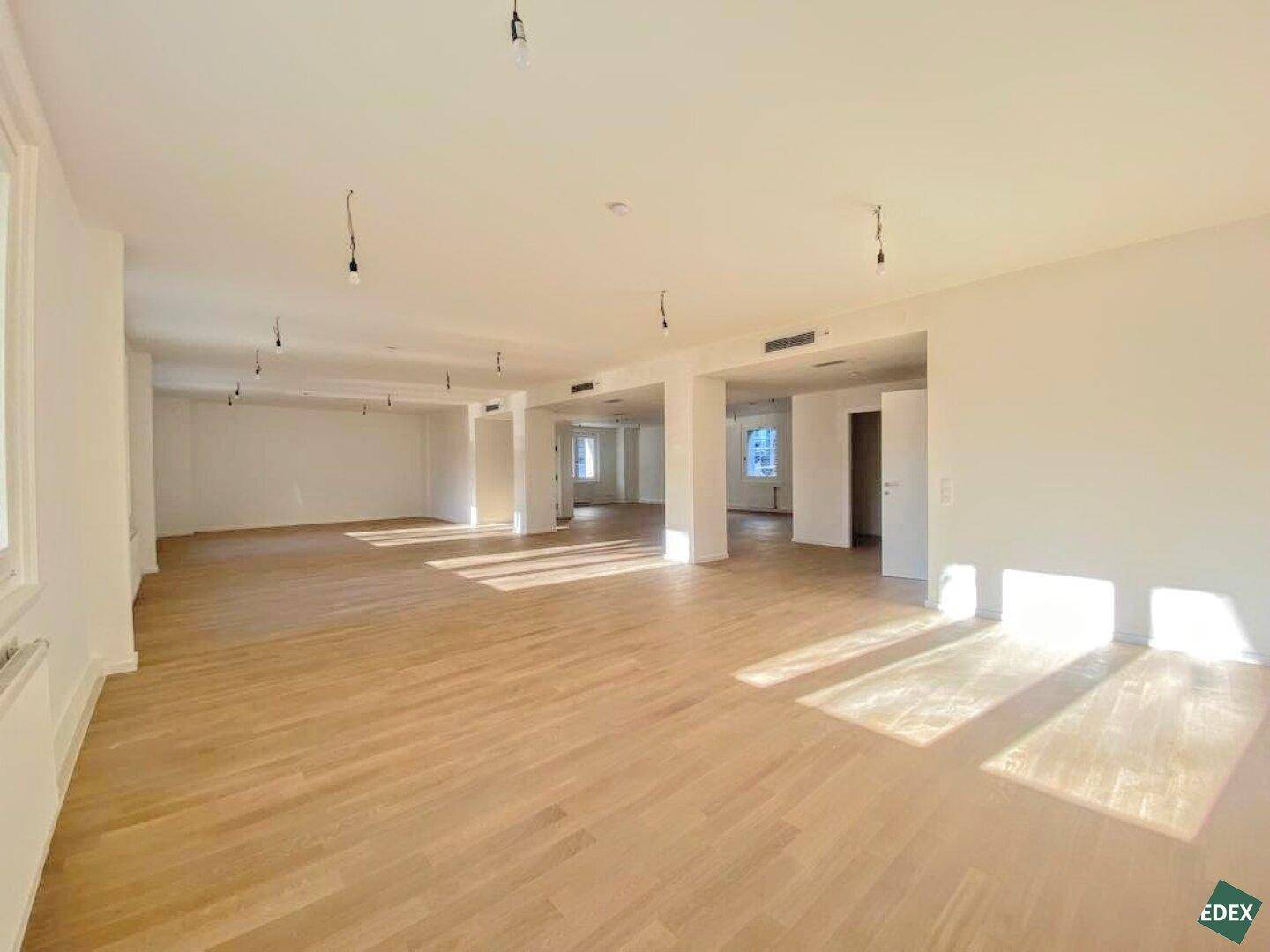 Großer, leerer Raum mit hellem Holzboden und viel Tageslicht, ideal für flexible Raumkonzepte.