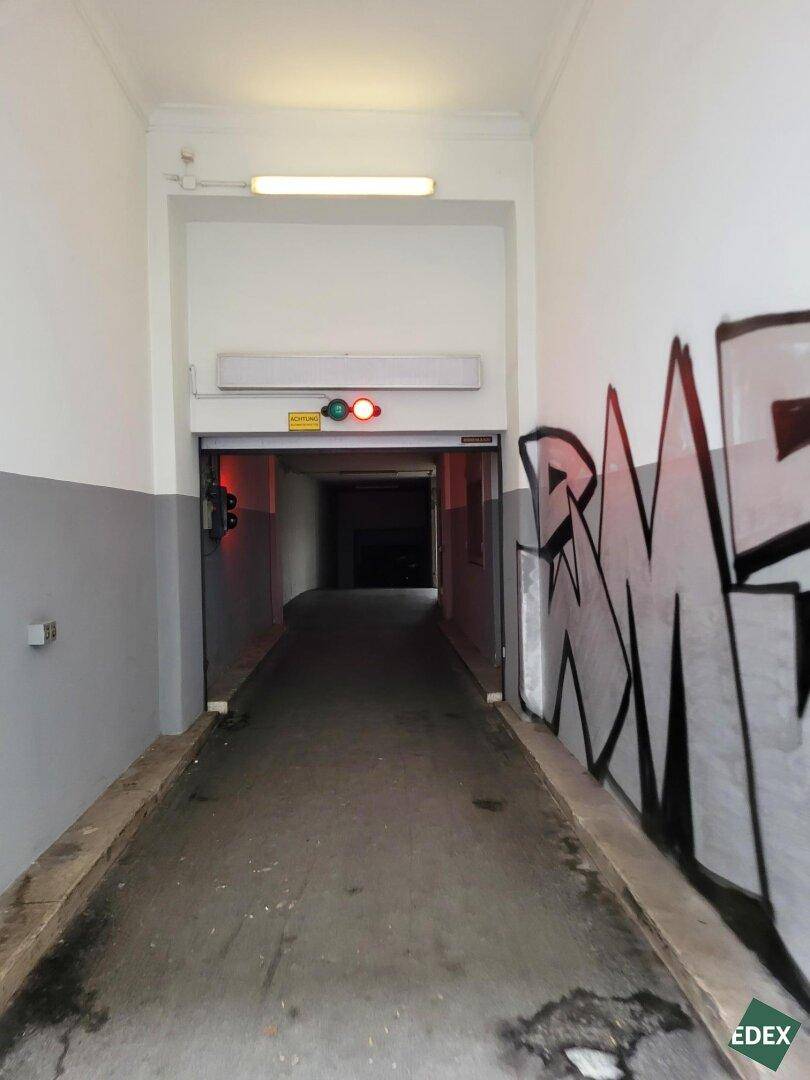 Blick in die Tiefgarage mit abfallender Rampe, Verkehrsampel und Graffiti an der Seitenwand.