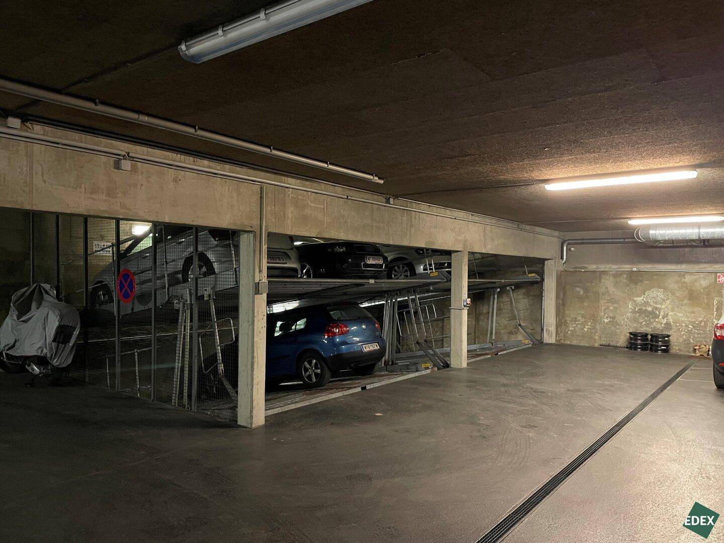 Übersicht der Tiefgarage mit mehreren Parklifts, auf denen Autos abgestellt sind, und einem breiten Fahrweg.