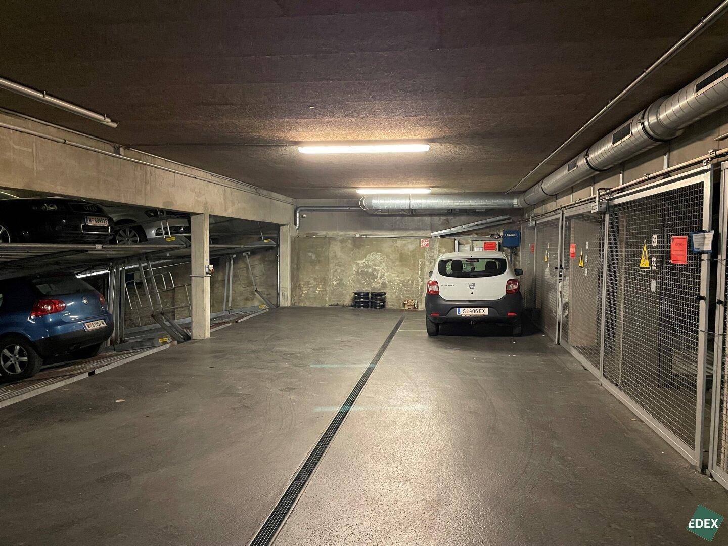 Geräumige Tiefgarage mit mehreren Parklifts, einem geparkten Auto und abschließbaren Lagerkäfigen.