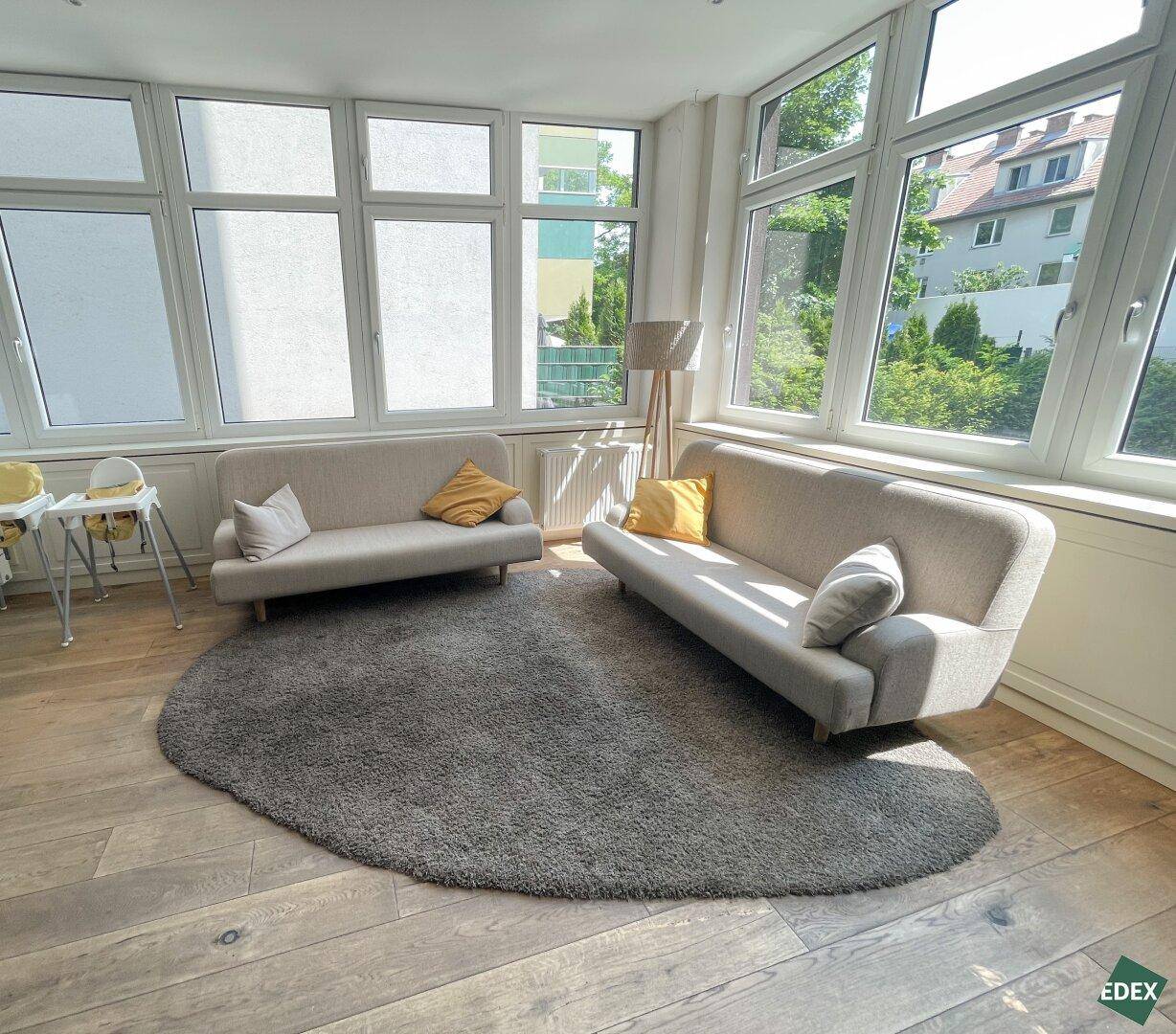 Heller Wintergarten mit großen Fenstern, zwei Sofas und Holzboden, bietet einen Blick ins Grüne.