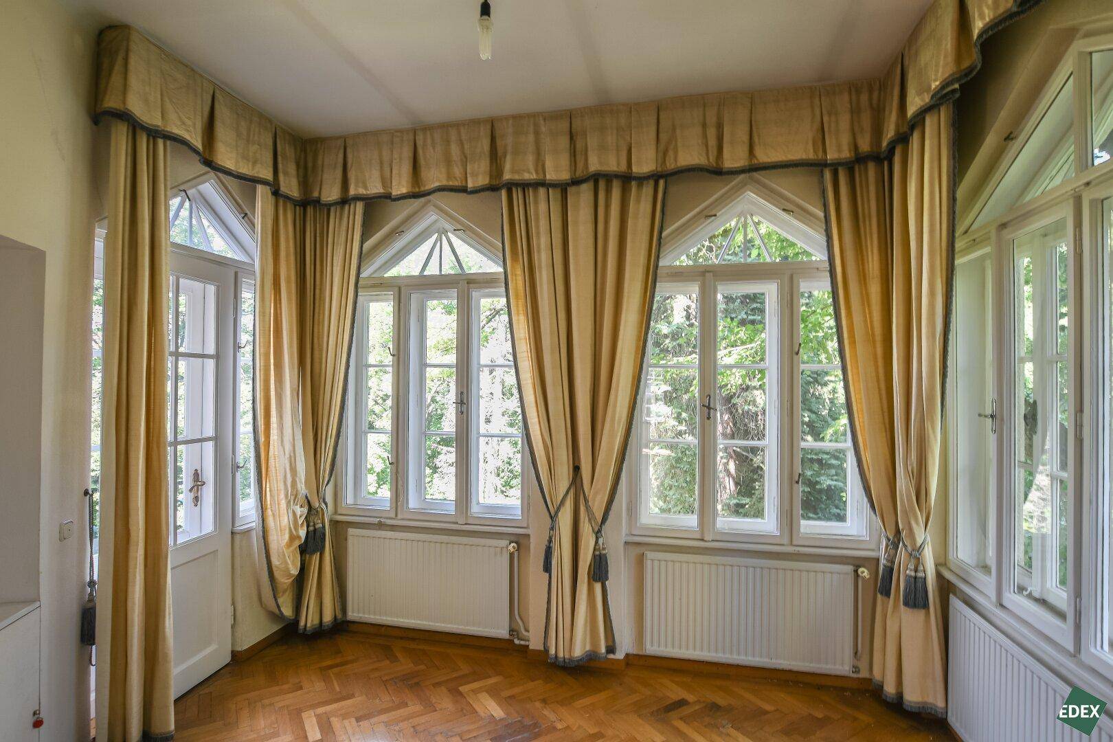 Geräumiges Zimmer mit eleganten Vorhängen, Fischgrätparkett und Blick ins Grüne.