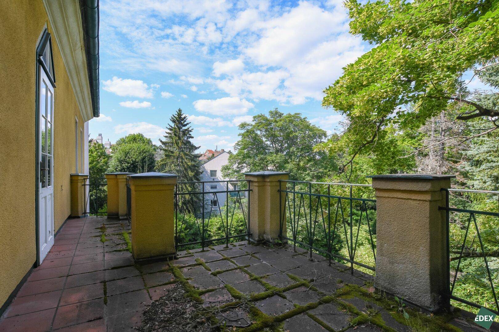 Große Terrasse mit alten Fliesen und schmiedeeisernem Geländer, umgeben von viel Grün.