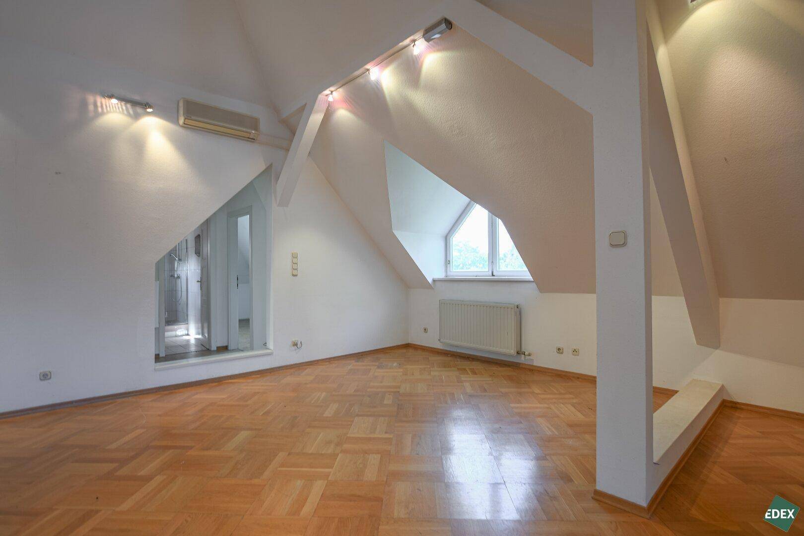 Helles Dachgeschosszimmer mit schrägen Wänden, Parkettboden und Dachfenster.