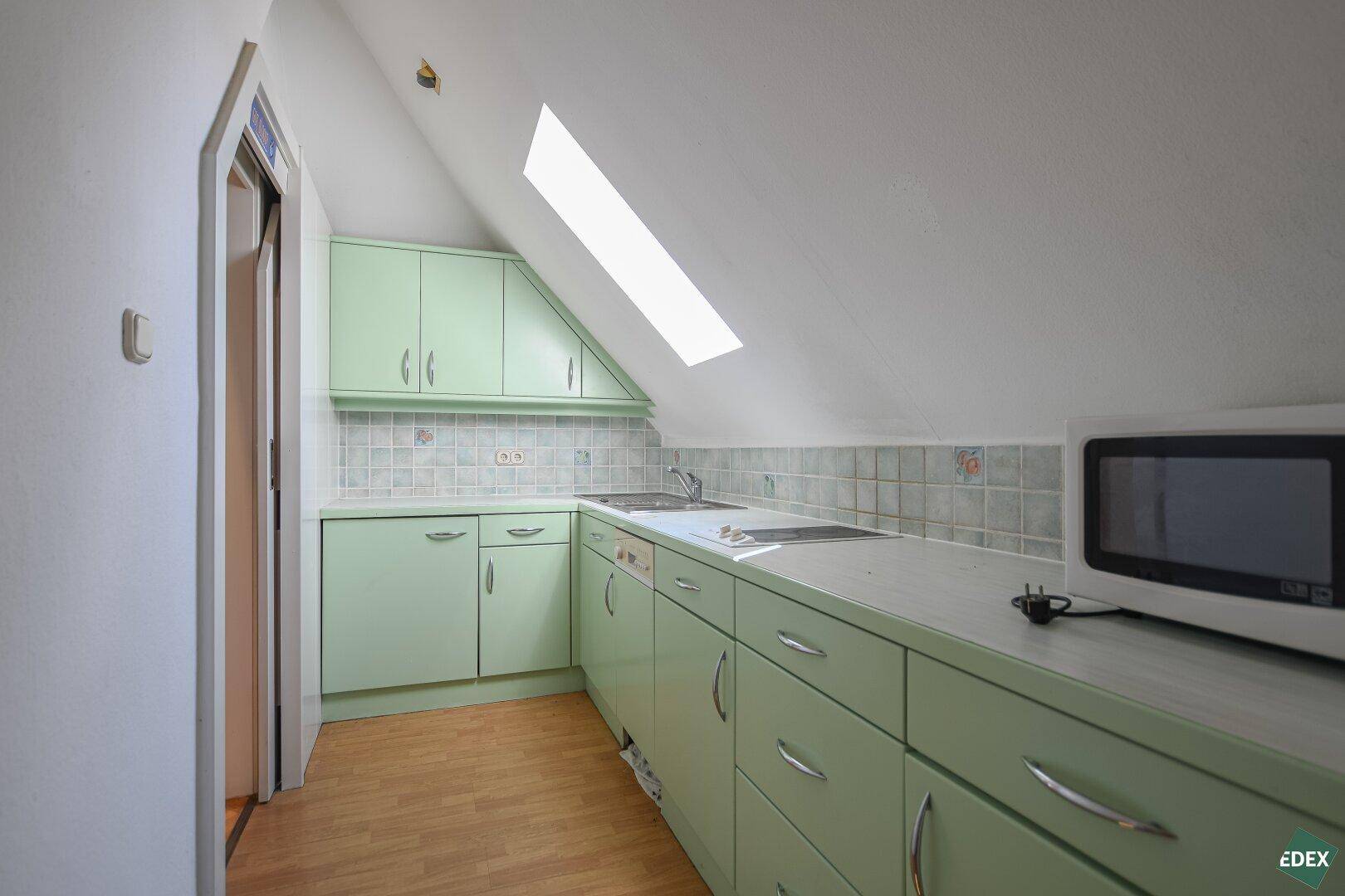 Kleine Dachgeschossküche mit grünen Schränken, Fliesenrückwand und Dachfenster.