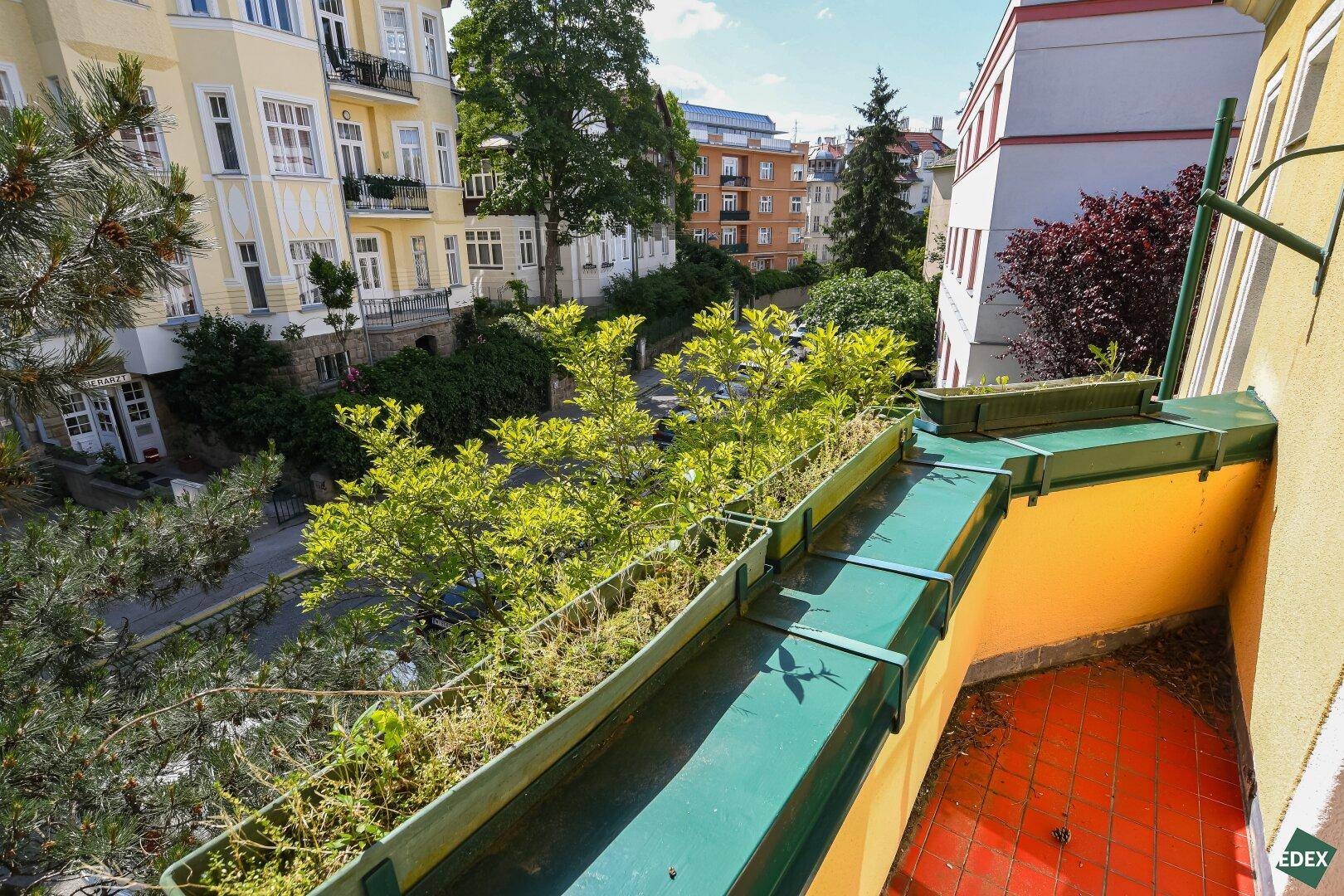 Kleiner Balkon mit Pflanzenkästen und Blick auf die Straße und umliegende Gebäude.