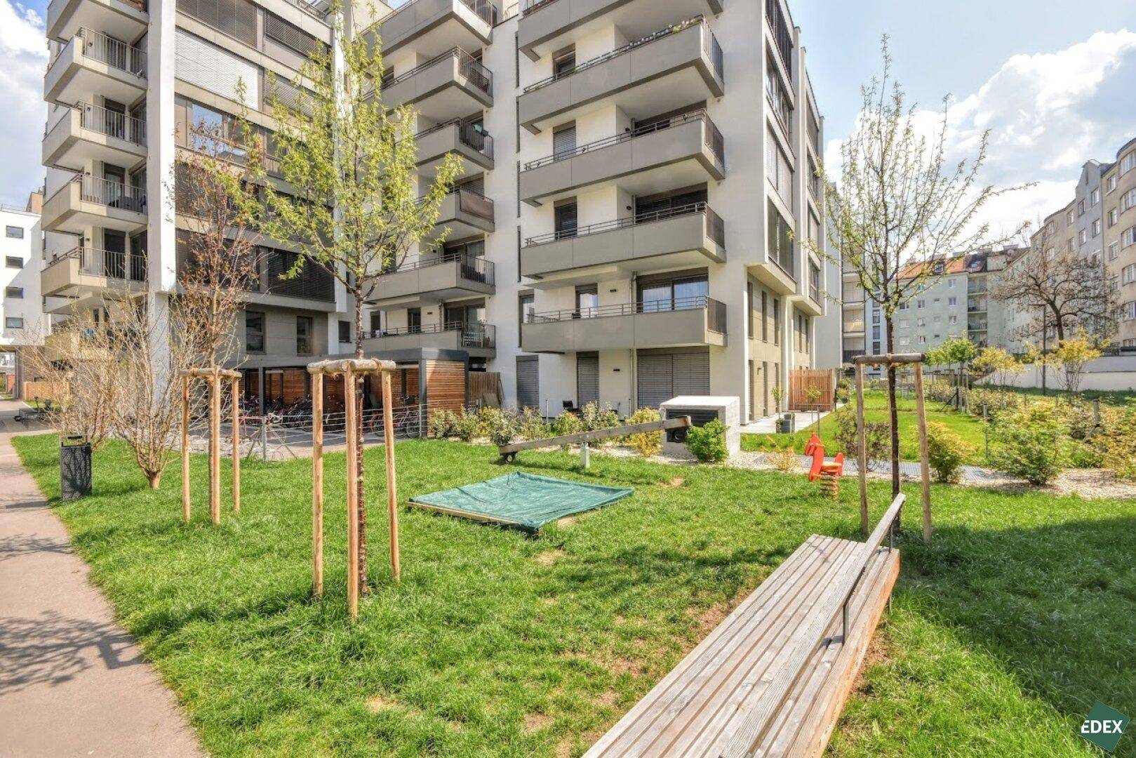 Gepflegte Grünfläche mit Spielplatz und Sitzgelegenheiten zwischen modernen Wohngebäuden.