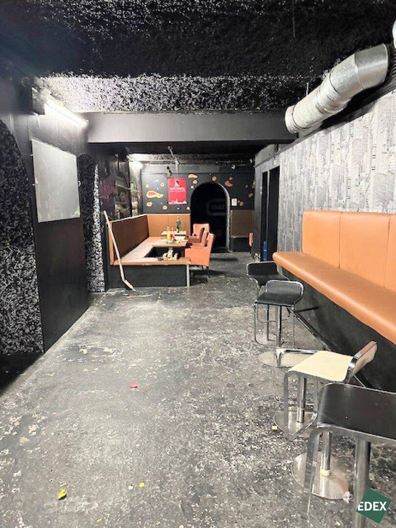 Großer Innenraum mit Sitzbänken, Tischen und dunklen Wänden, der als Lounge-Bereich dient.