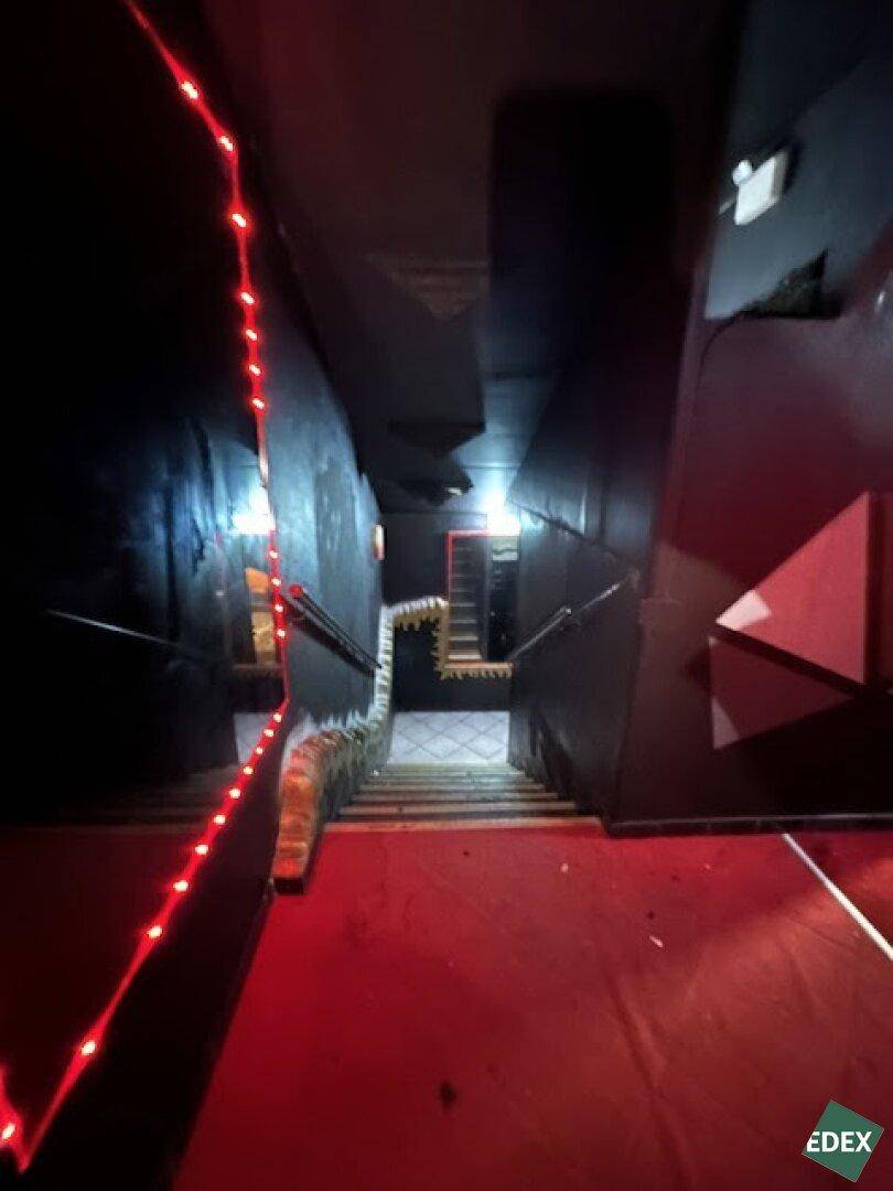 Treppenhaus mit rotem Teppich, dunklen Wänden und roten LED-Lichtern entlang des Geländers.