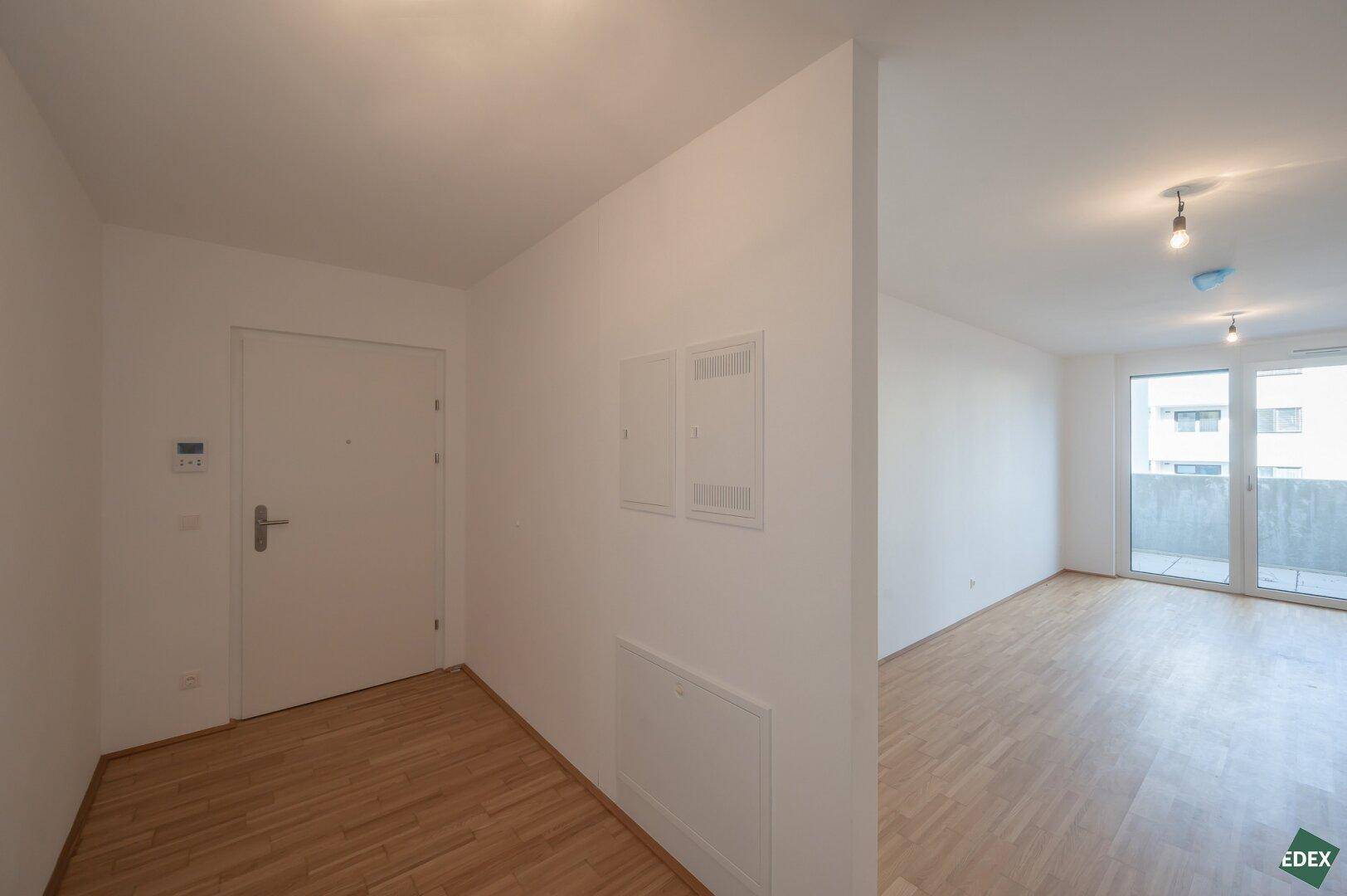 Heller Eingangsbereich mit Parkettboden und weißer Tür, der zu den Wohnräumen führt.