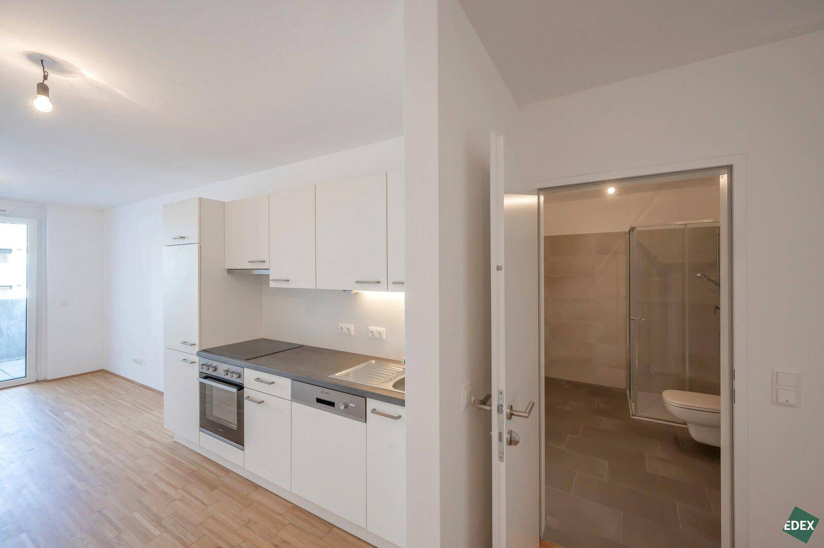 Moderne Einbauküche mit weißen Schränken und integrierten Geräten, angrenzend an ein Badezimmer.