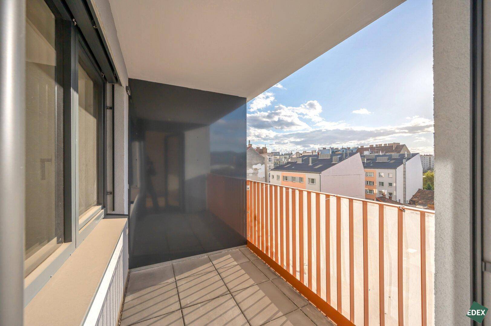 Sonniger Balkon mit Stadtblick und orangefarbenem Geländer, perfekt für den Morgenkaffee.