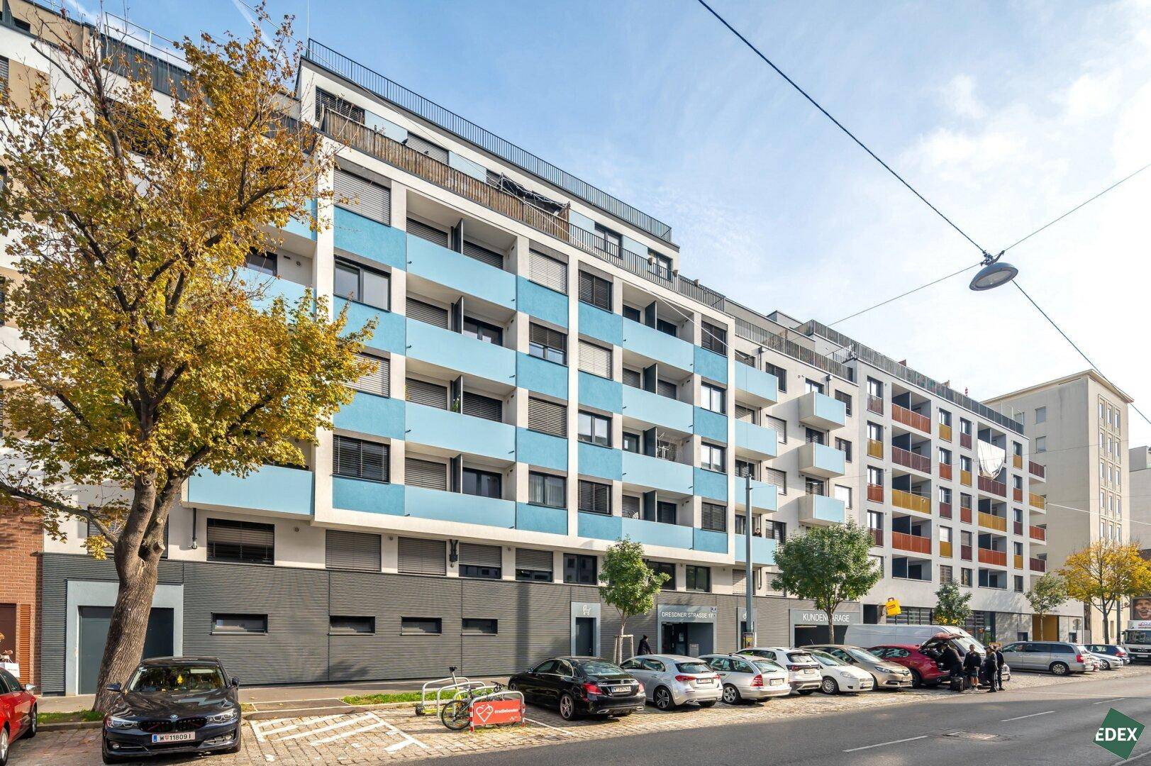 Moderne Wohngebäude mit blauen Balkonen und großen Fenstern entlang einer städtischen Straße.