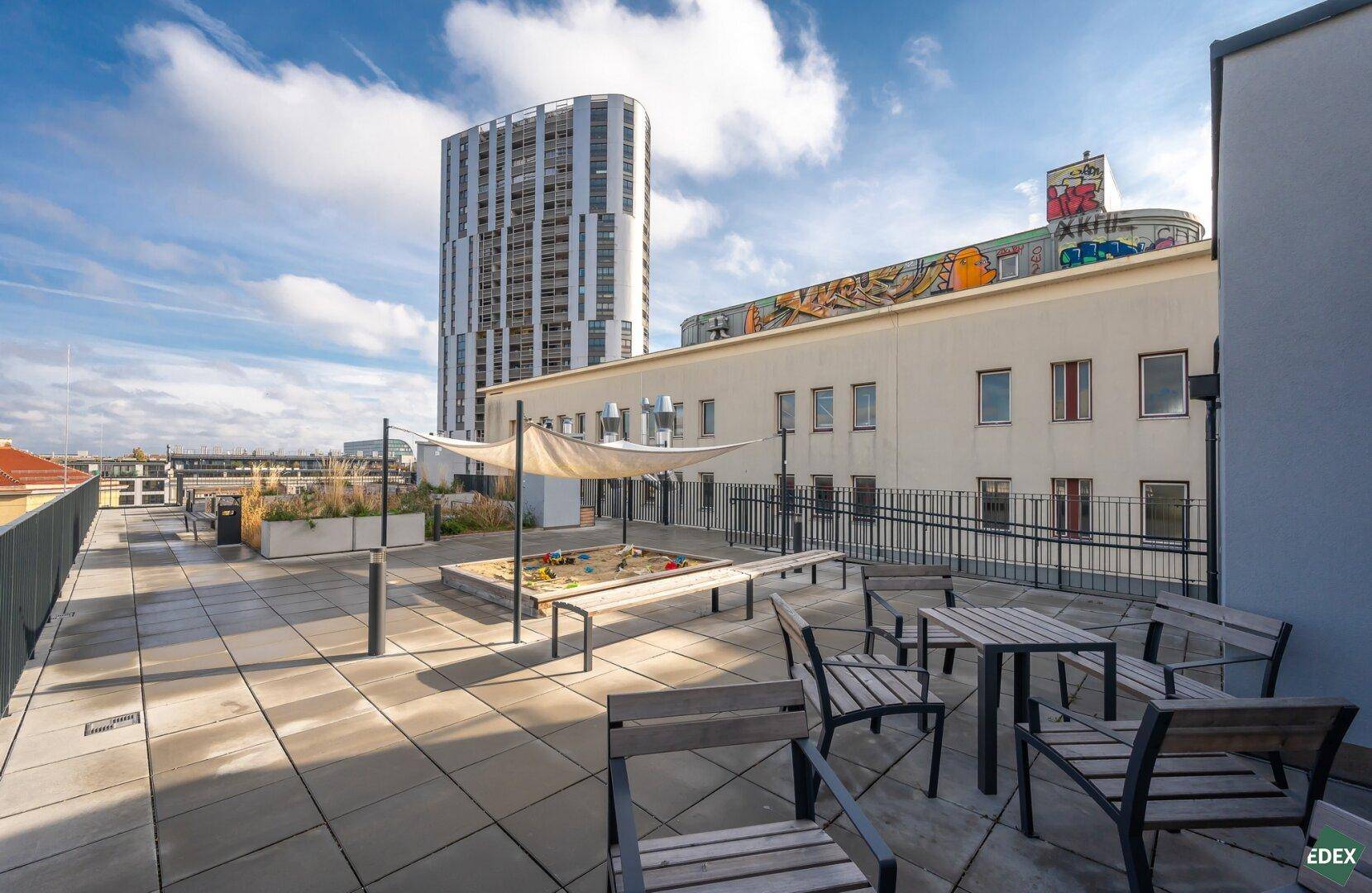 Gemeinschaftliche Dachterrasse mit Sandkasten, Sitzgelegenheiten und weitem Blick über die Stadt.