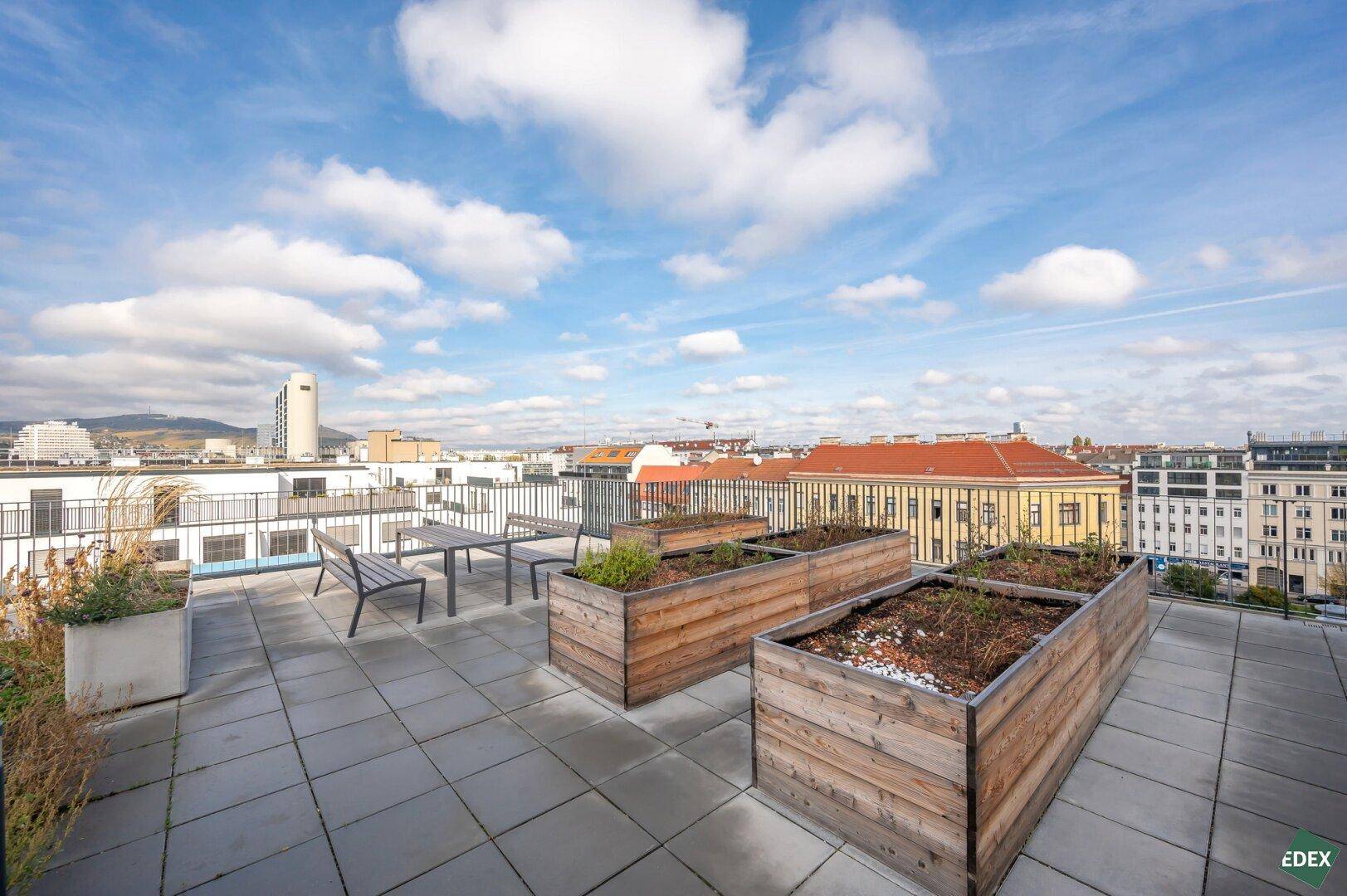 Dachterrasse mit Hochbeeten und Tischen, bietet einen weiten Blick über die städtische Umgebung.