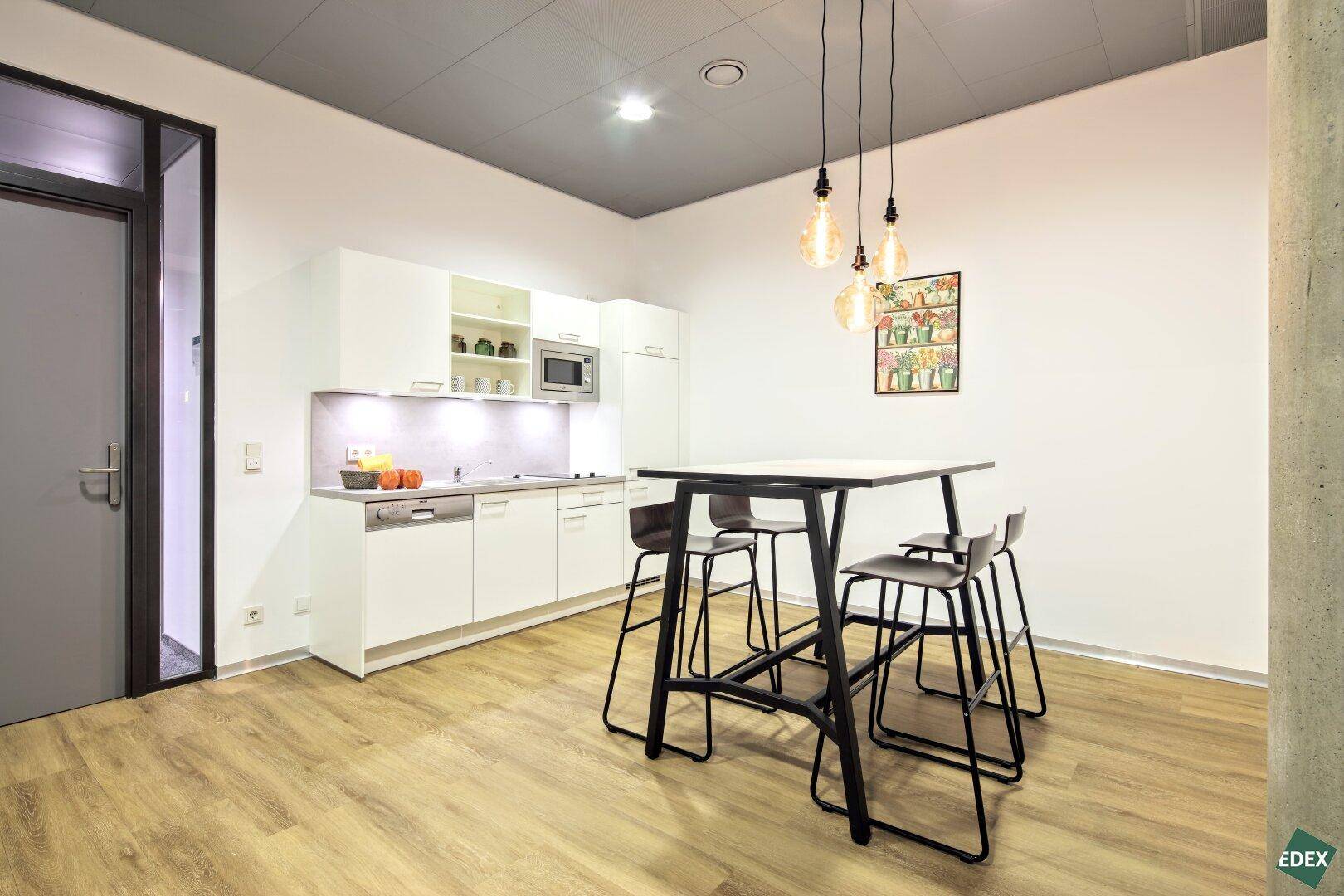 Moderne Teeküche mit weißen Schränken, Holzboden und Stehtisch, perfekt für Pausen im Büro.