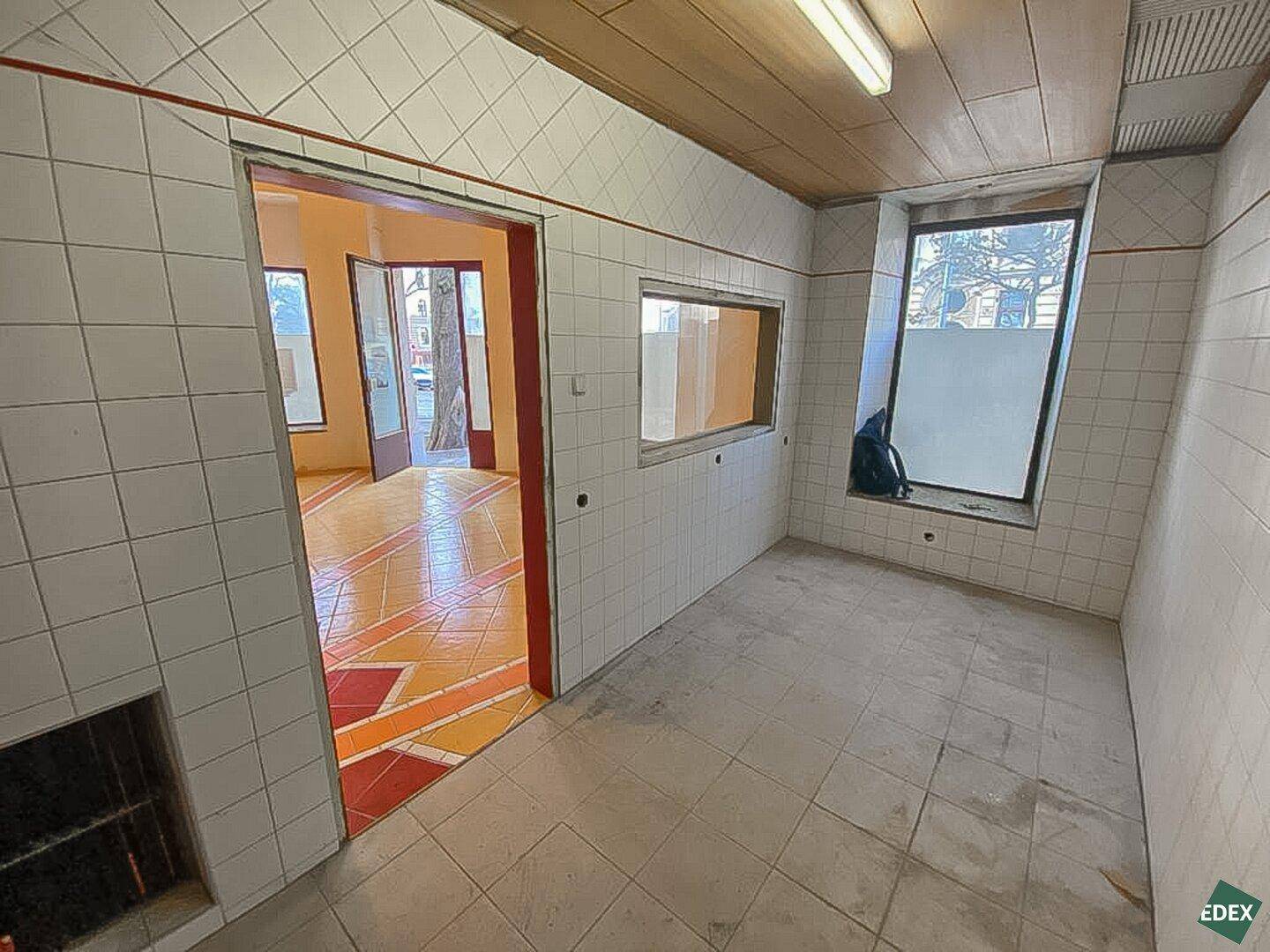 Gefliester Funktionsraum mit Holzdecke, einer Durchreiche und Blick in einen angrenzenden Bereich mit gemustertem Boden.