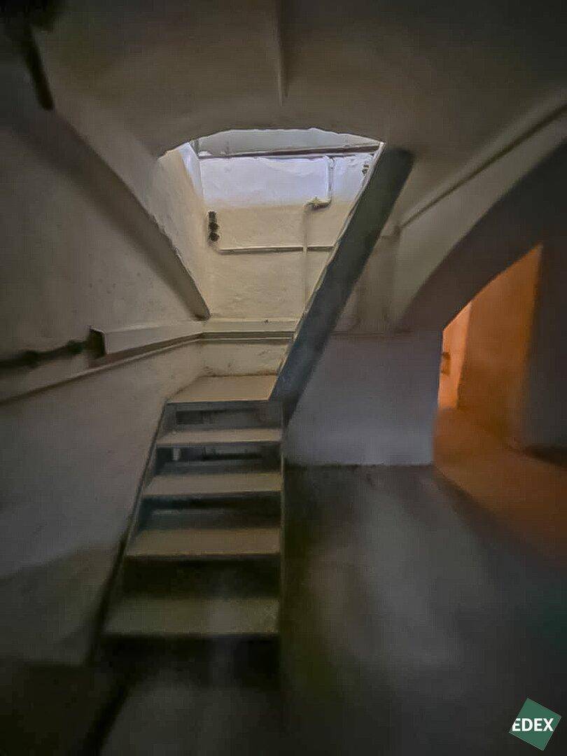 Dunkler Kellerbereich mit einer einfachen Holztreppe und gewölbten Decken, die zu einem oberen Bereich führt und Sanierung benötigt.