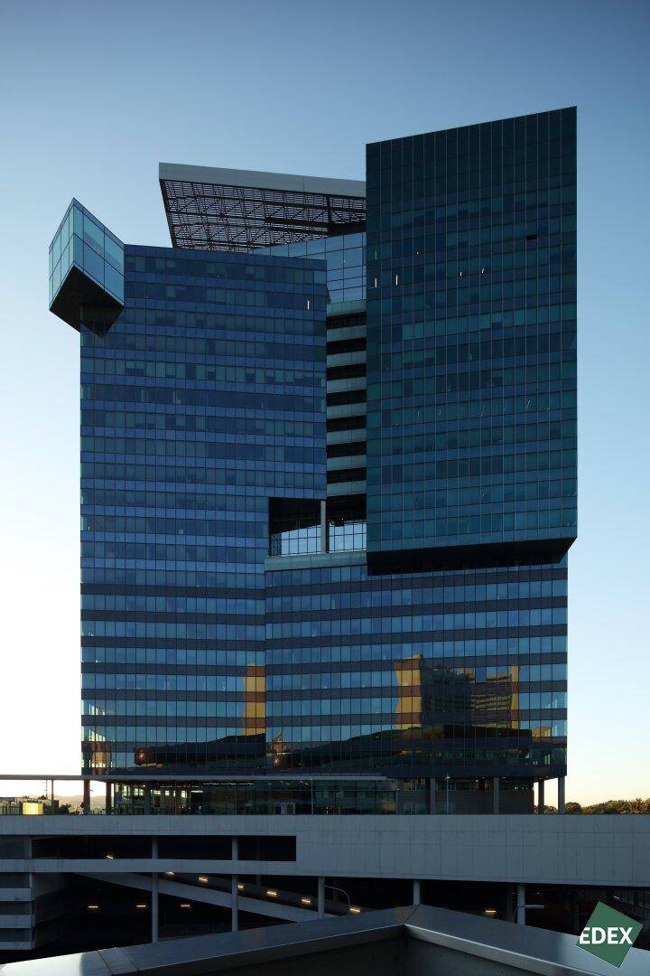 Modernes Hochhaus mit blauer Glasfassade bei Sonnenuntergang, das die Umgebung widerspiegelt.