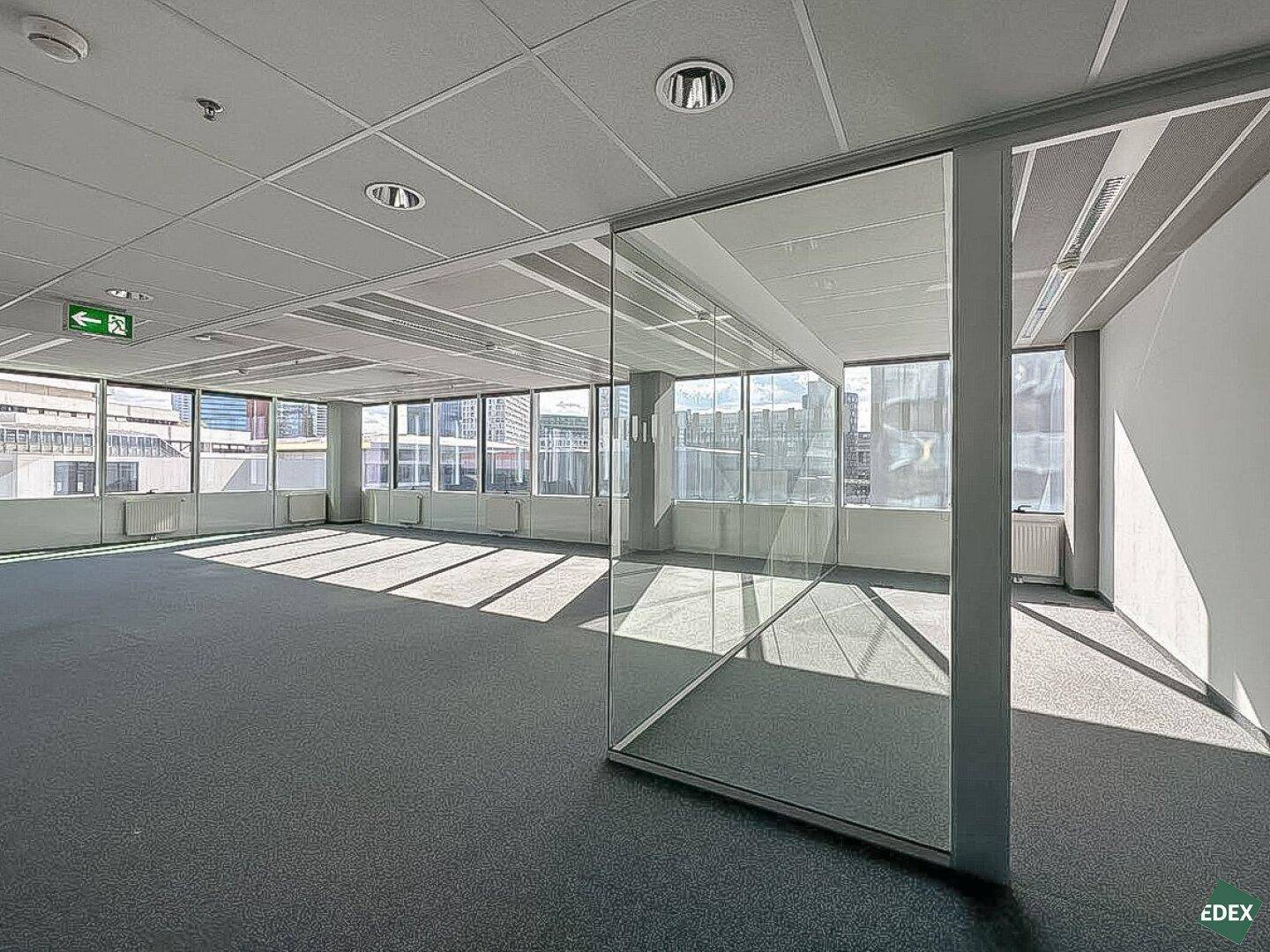 Geräumiges, leeres Büro mit Teppichboden und Glaswänden, das viel Tageslicht und eine flexible Raumgestaltung bietet.