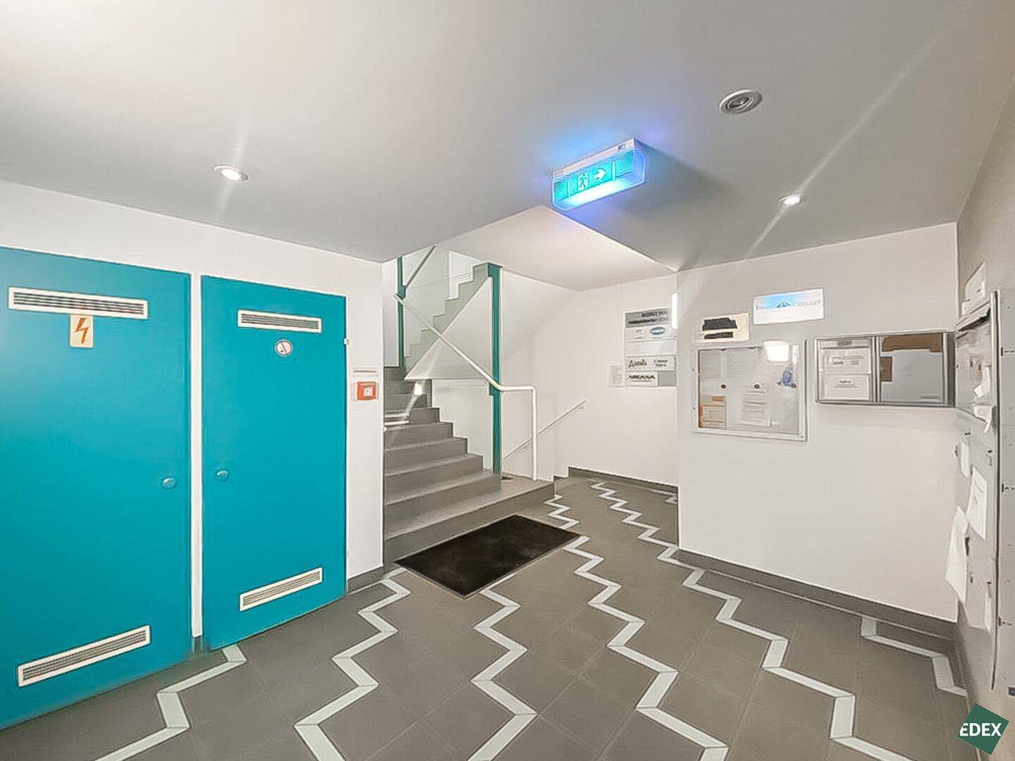 Eingangsbereich mit Treppenaufgang, auffälligen blauen Türen und gemustertem Fliesenboden.
