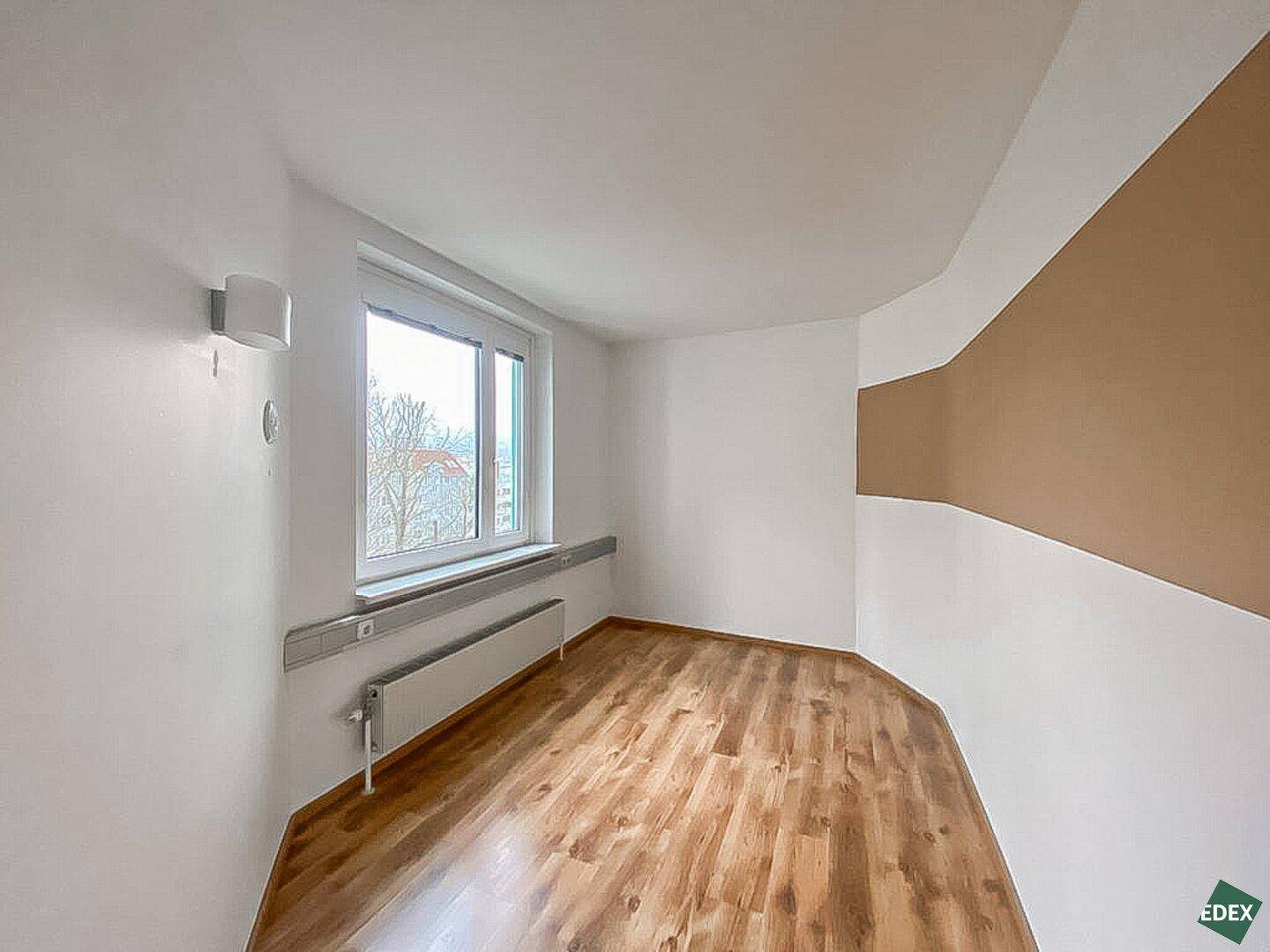 Helles Büro mit Holzfußboden, großem Fenster und einer geschwungenen beigen Akzentwand.