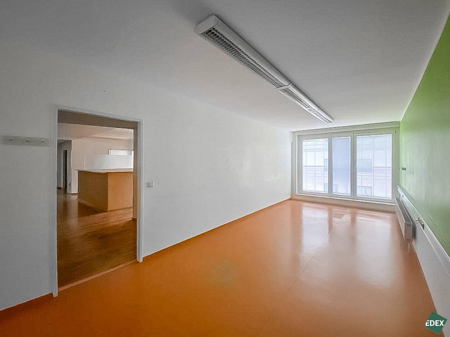 Büro mit leuchtend orangefarbenem Boden, großen Fenstern und Blick in einen weiteren Raum.