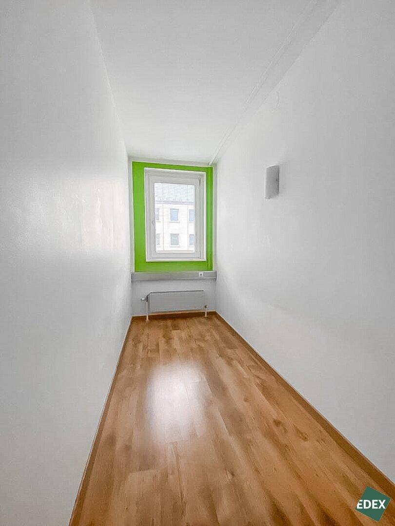 Schmaler Büroraum mit Holzfußboden, einem Fenster und einer grünen Akzentwand.