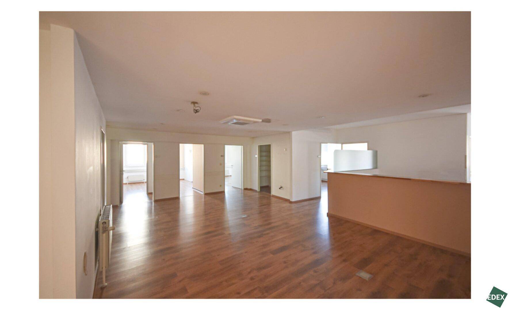 Geräumiger offener Bürobereich mit hellem Holzfußboden und einer Empfangstheke, ideal für flexible Arbeitsplätze.