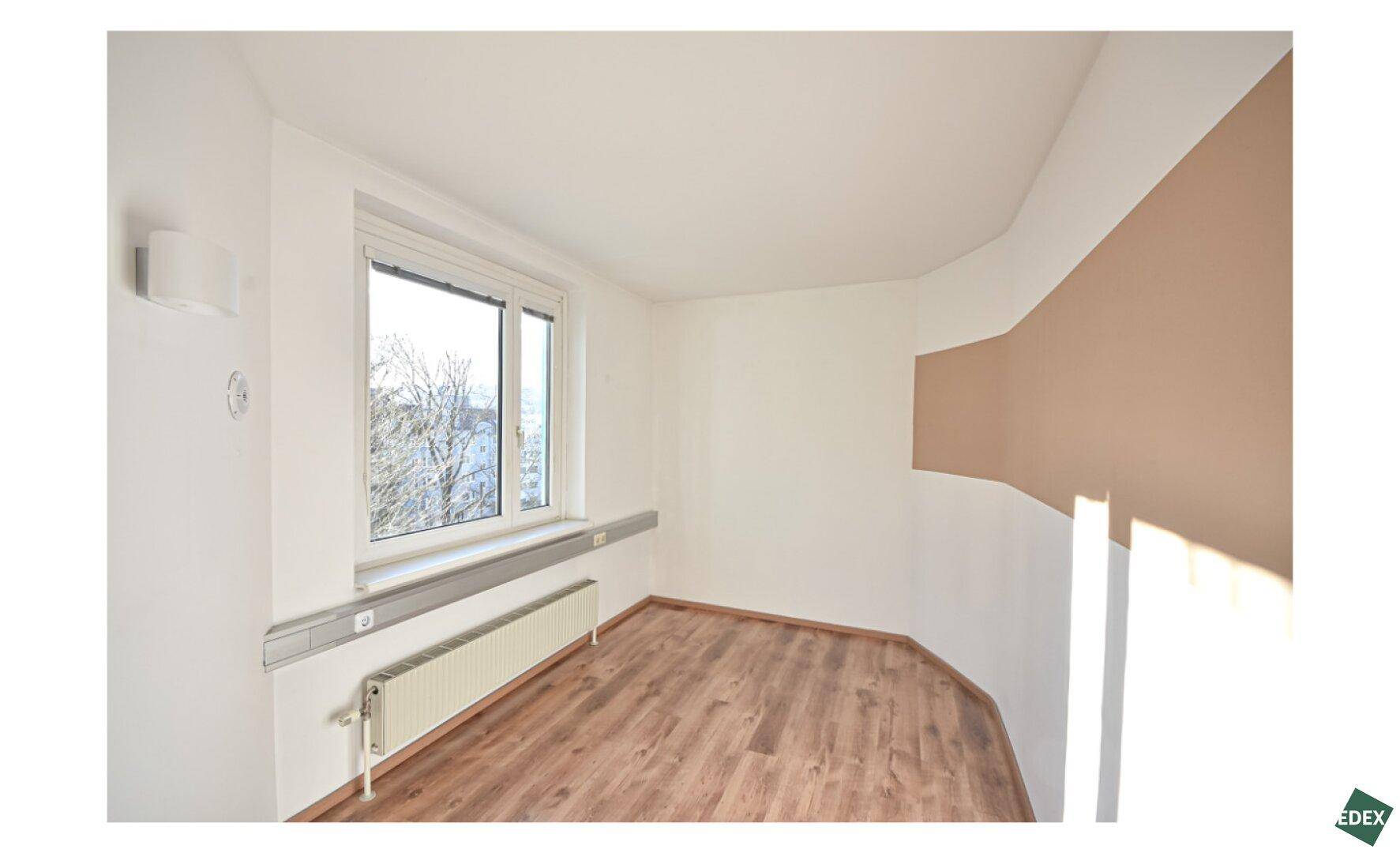 Helles Büro mit Holzfußboden, großem Fenster und einer geschwungenen beigen Akzentwand.