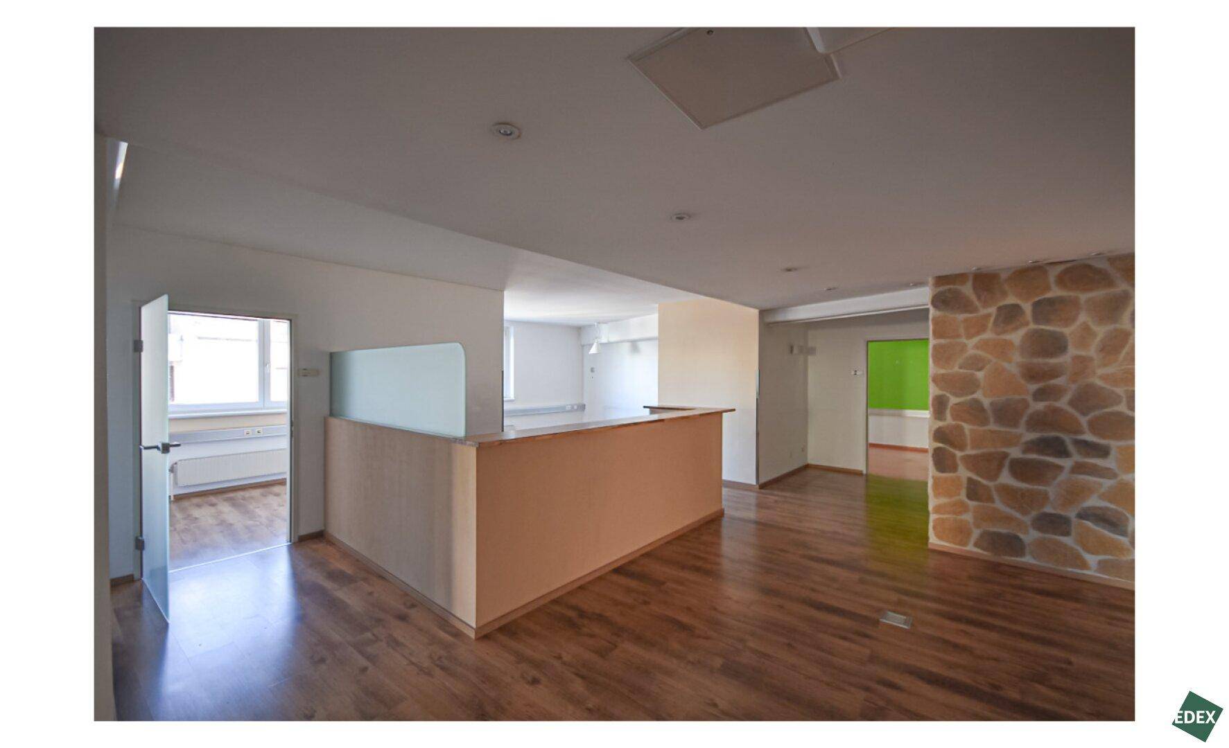 Offener Bürobereich mit rustikaler Steinwand, Holzfußboden und einer Empfangstheke.