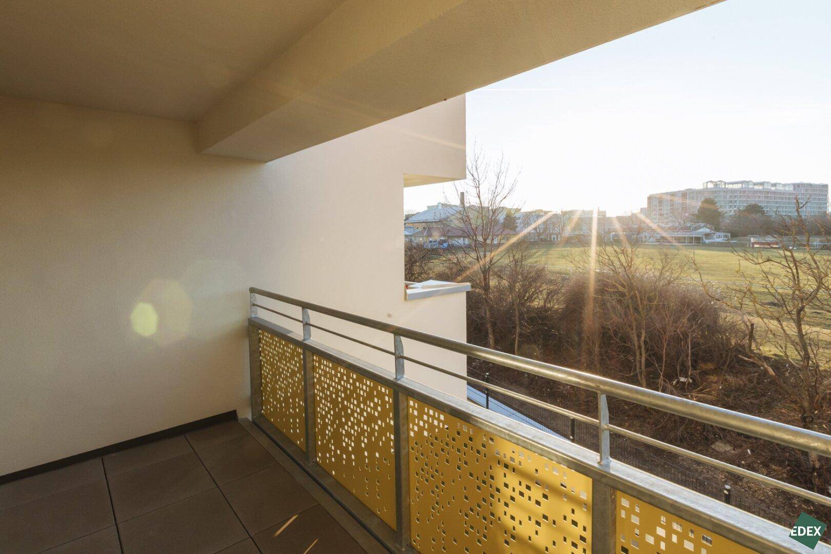Sonniger Balkon mit gelochtem Geländer und weitem Blick auf die Landschaft.