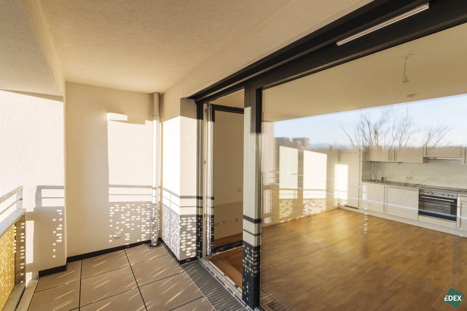 Heller Wohnbereich mit Zugang zum Balkon und Blick auf die offene Küche.