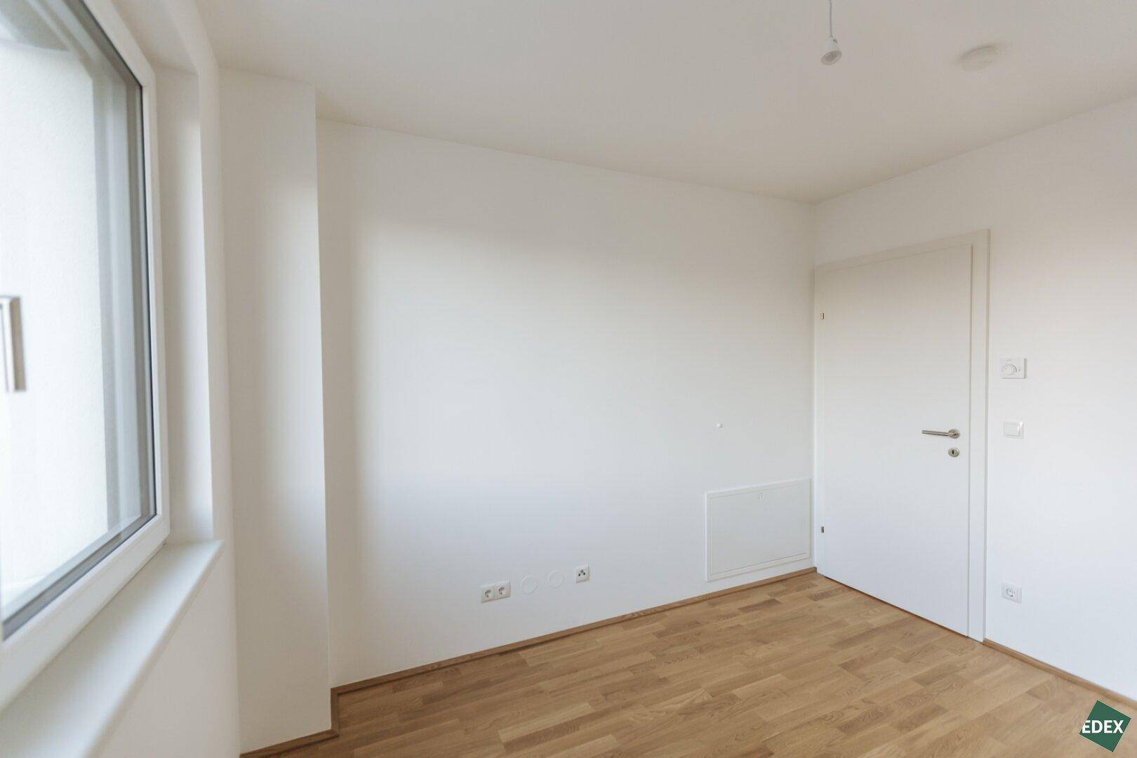 Helles Schlafzimmer mit Holzboden und einem Fenster, bereit zur Einrichtung.