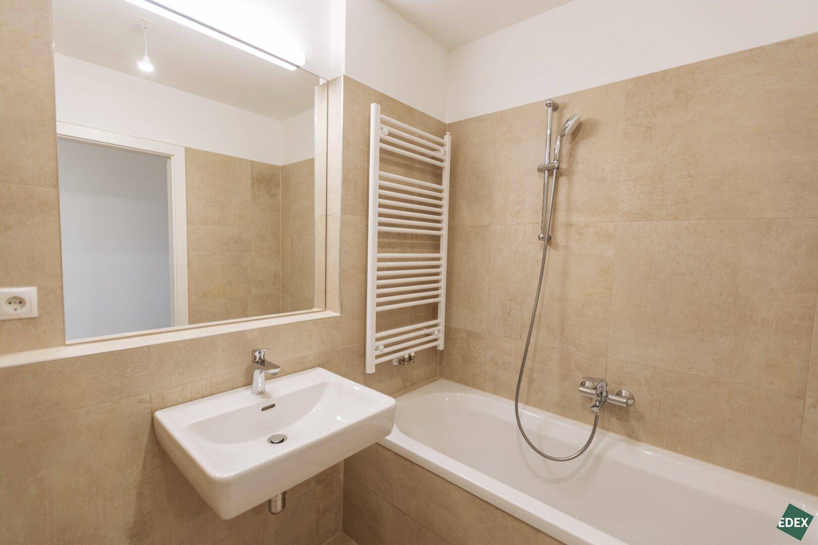 Modernes Badezimmer mit Badewanne, Waschbecken und beheiztem Handtuchhalter.