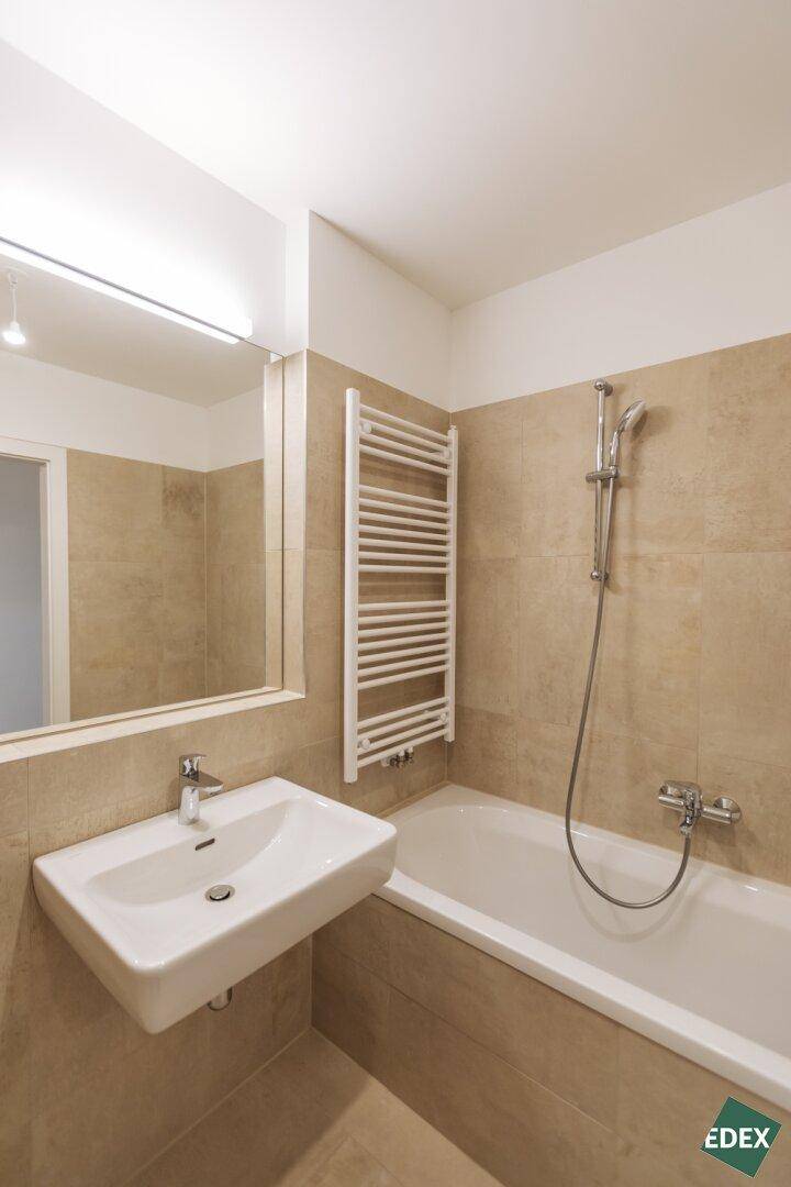 Helles Badezimmer mit beigefarbenen Fliesen, Badewanne und modernem Waschbecken.