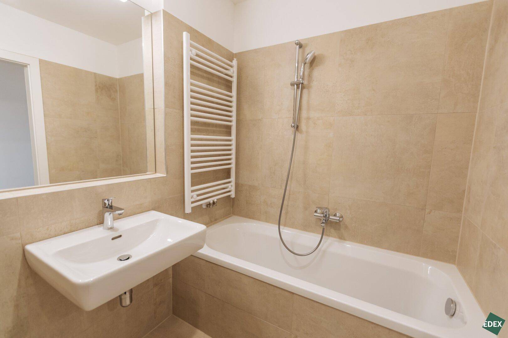 Funktionales Badezimmer mit Badewanne, Waschbecken und beheiztem Handtuchhalter.