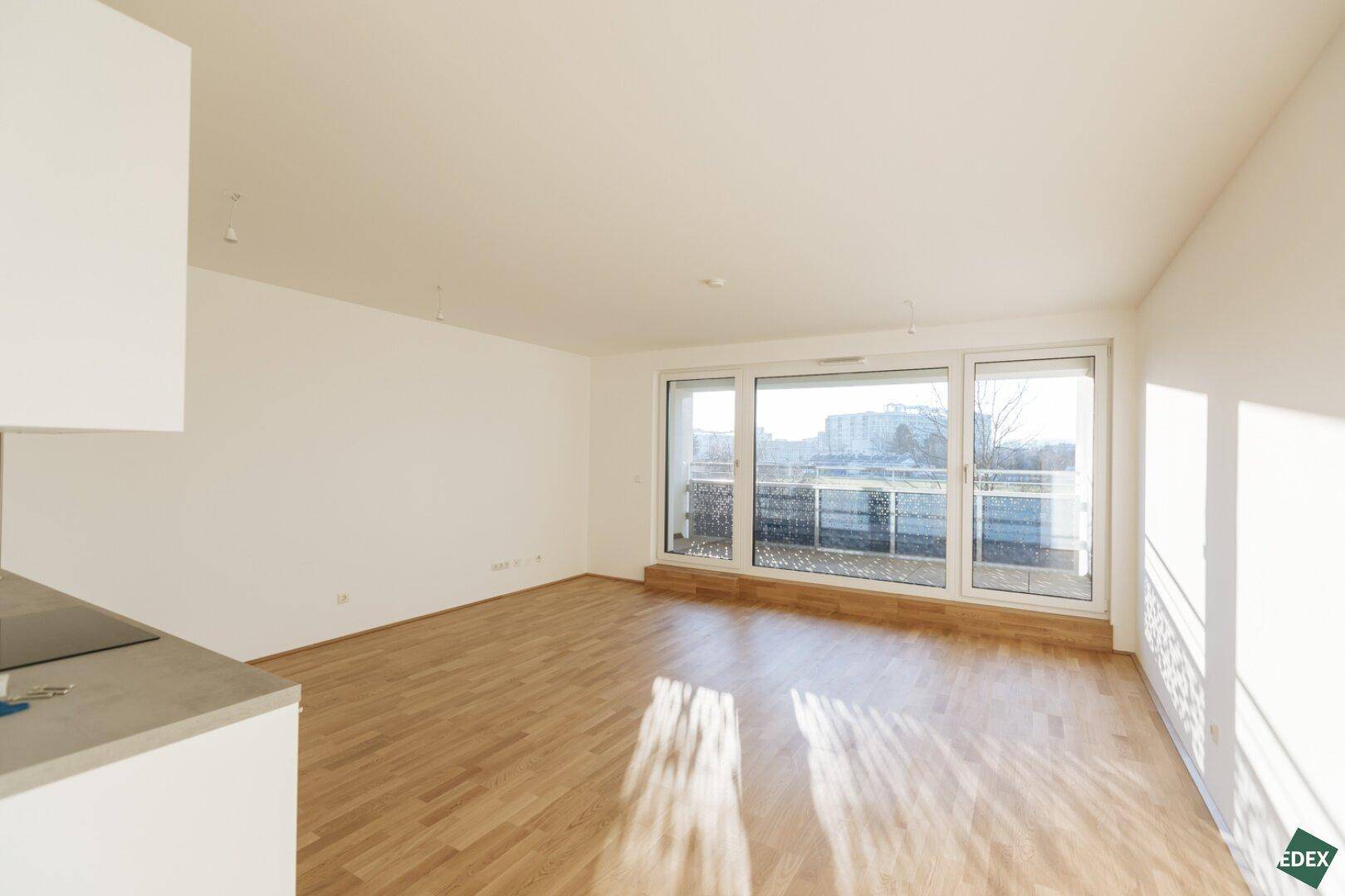 Lichtdurchfluteter Wohnraum mit großen Fenstern und Holzboden.