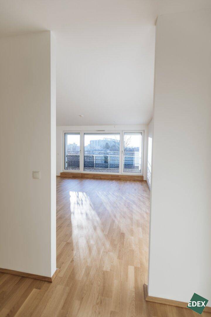 Heller, leerer Wohnraum mit großen Fenstern und Holzboden.