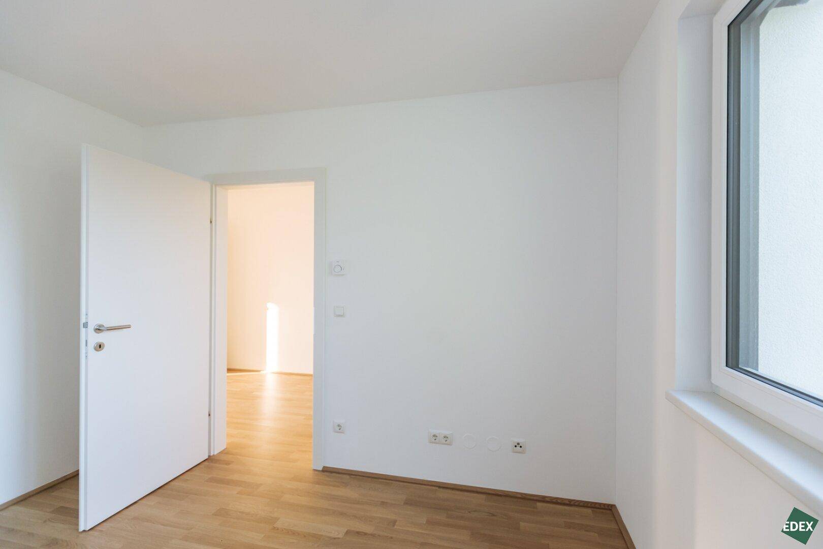 Helles Zimmer mit Holzboden, Fenster und offener Tür.
