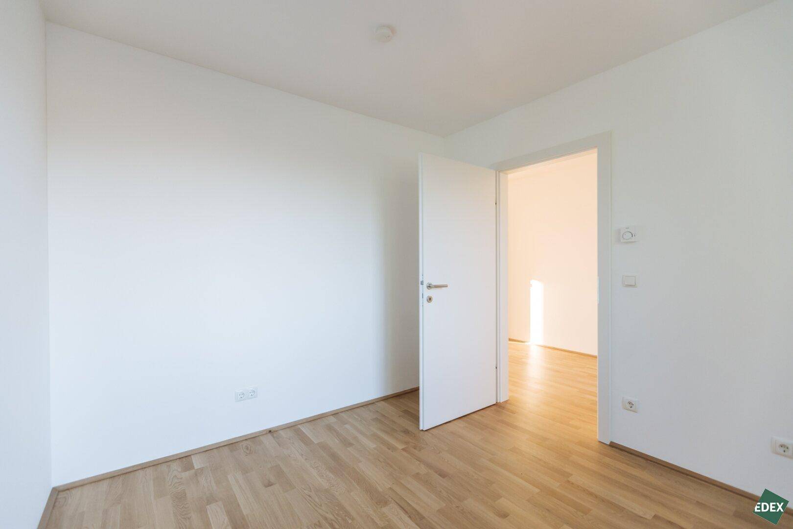Helles Zimmer mit Holzboden und offener Tür, bereit zum Einrichten.