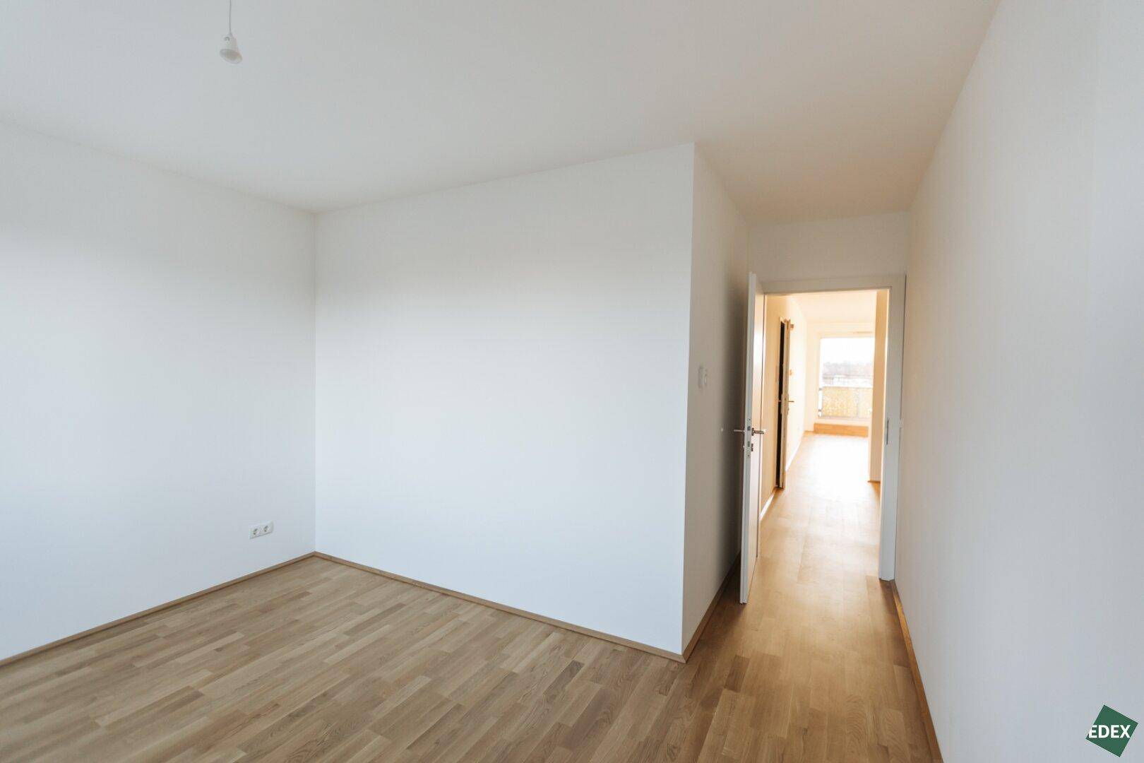 Leerer Raum mit Holzboden und Blick in den Flur sowie zu einem weiteren Zimmer.