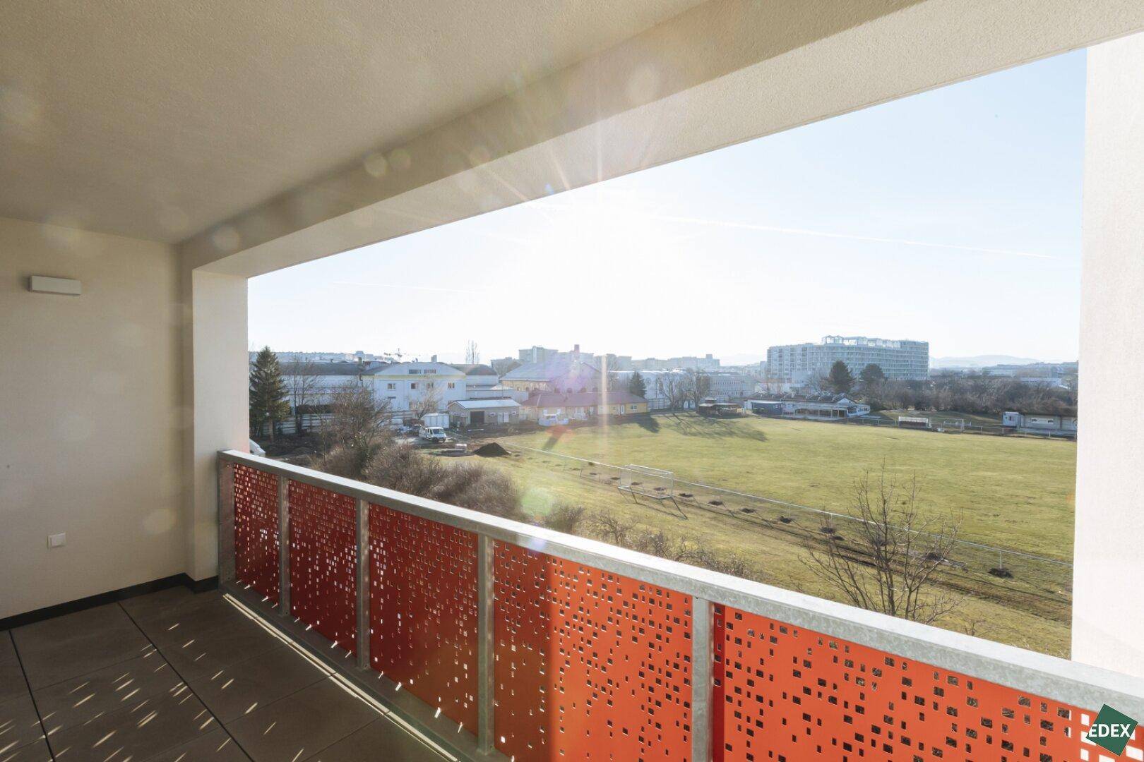 Sonniger Balkon mit Blick auf grüne Wiesen und die umliegende Bebauung.