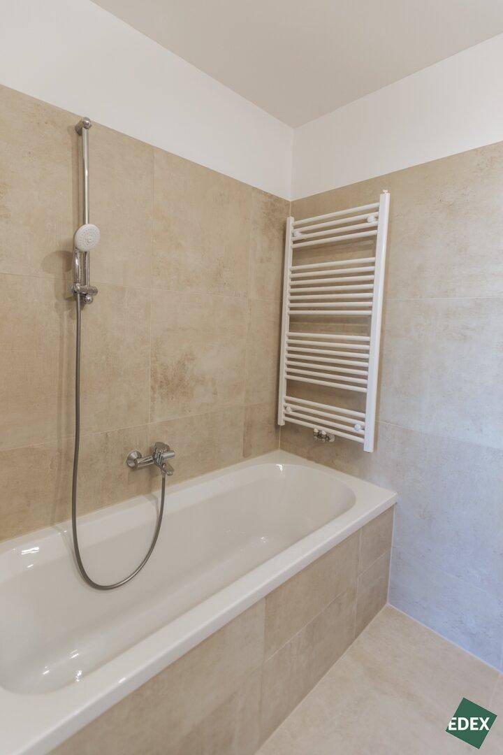 Modernes Badezimmer mit beigefarbenen Fliesen, Badewanne und beheiztem Handtuchhalter.