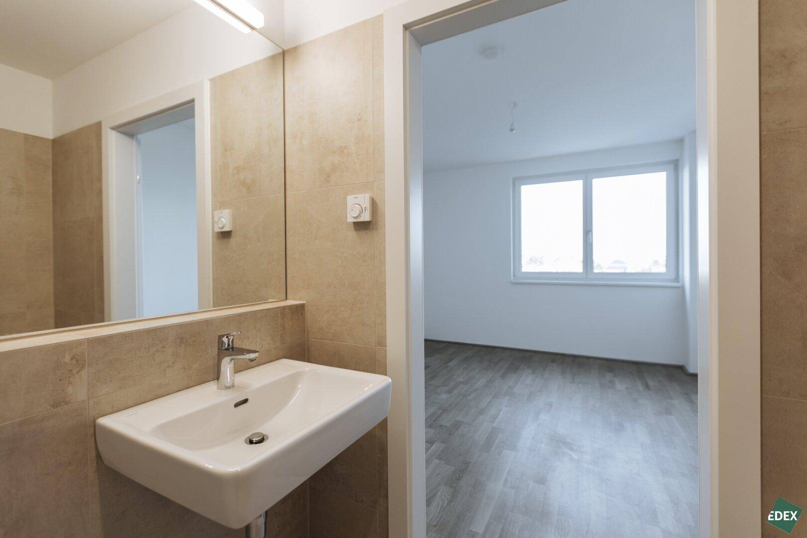Modernes Badezimmer mit Waschbecken, großem Spiegel und beigefarbenen Fliesen.