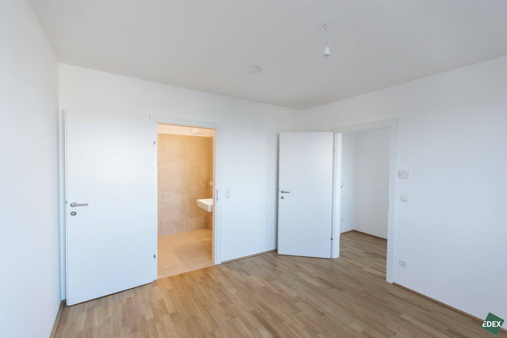 Helles Zimmer mit Parkettboden und Zugang zu einem modernen Badezimmer.
