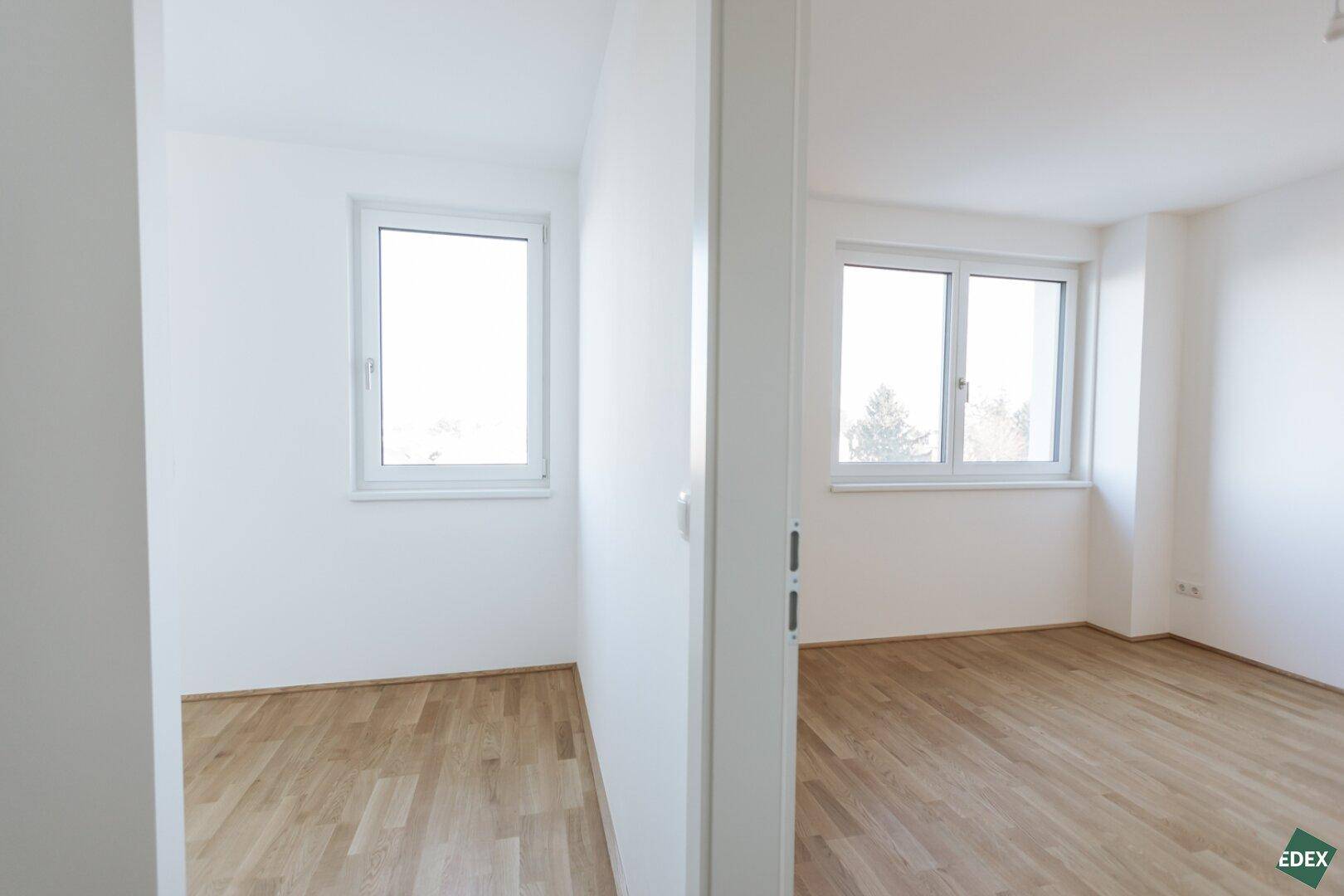 Blick vom Flur in zwei helle Zimmer mit Parkettboden und Fenstern.