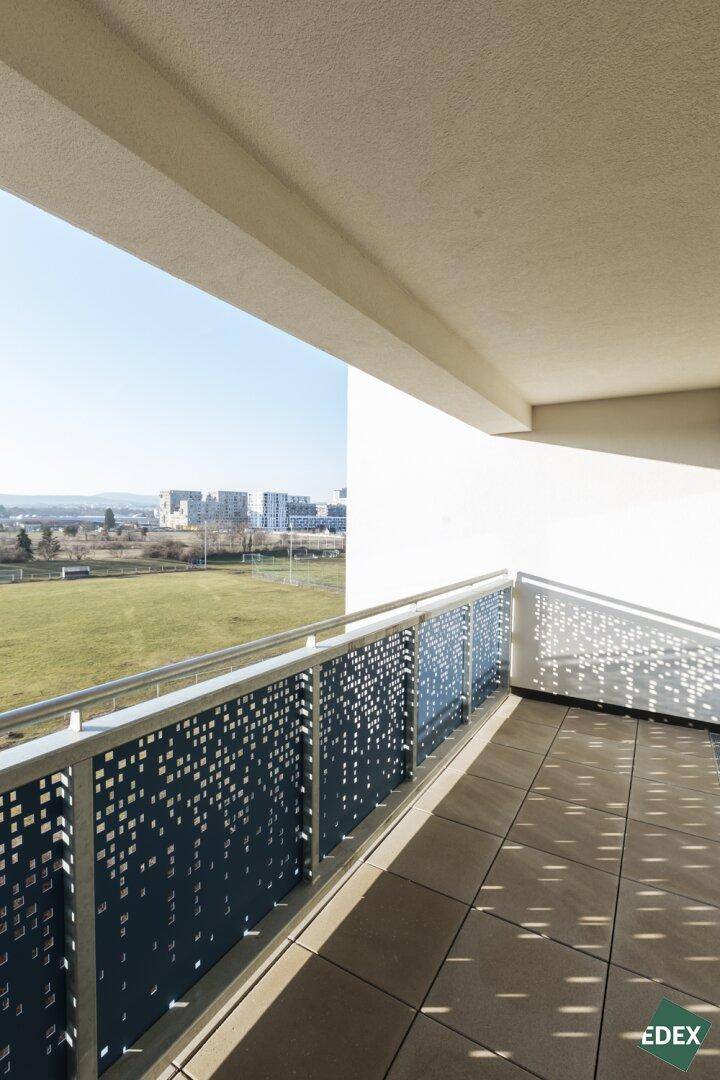 Geräumiger Balkon mit moderner Lochblech-Brüstung und weitem Blick über grüne Felder.