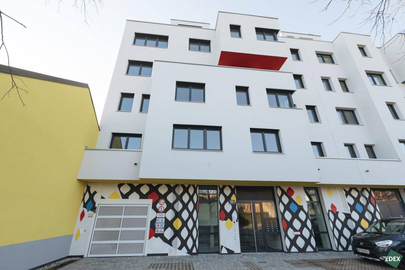Moderne Wohnanlage mit farbenfroher Fassadengestaltung und Tiefgaragenzufahrt.